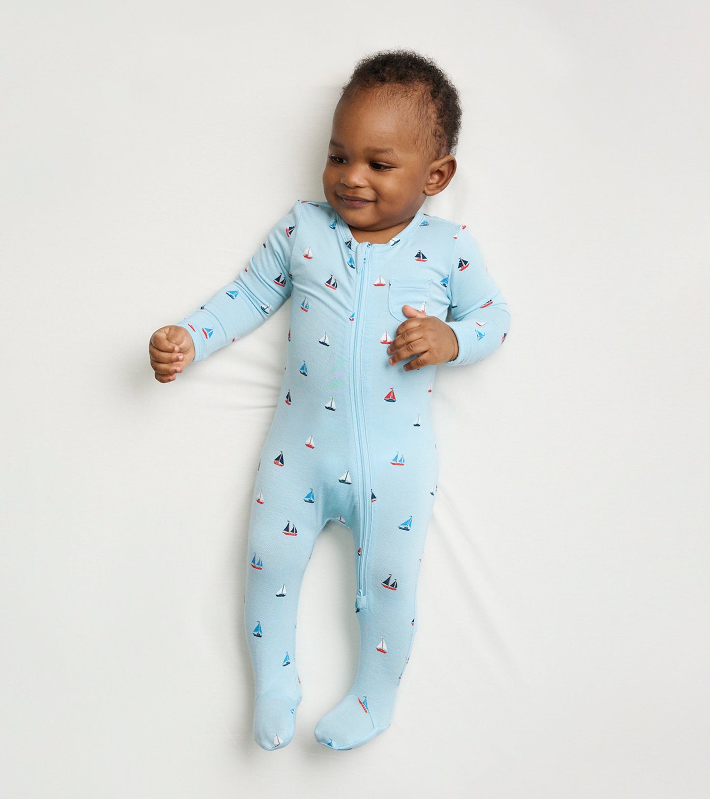 Light blue footed sleeper with tiny sailboat patterns, featuring a front zipper and long sleeves for baby boys.