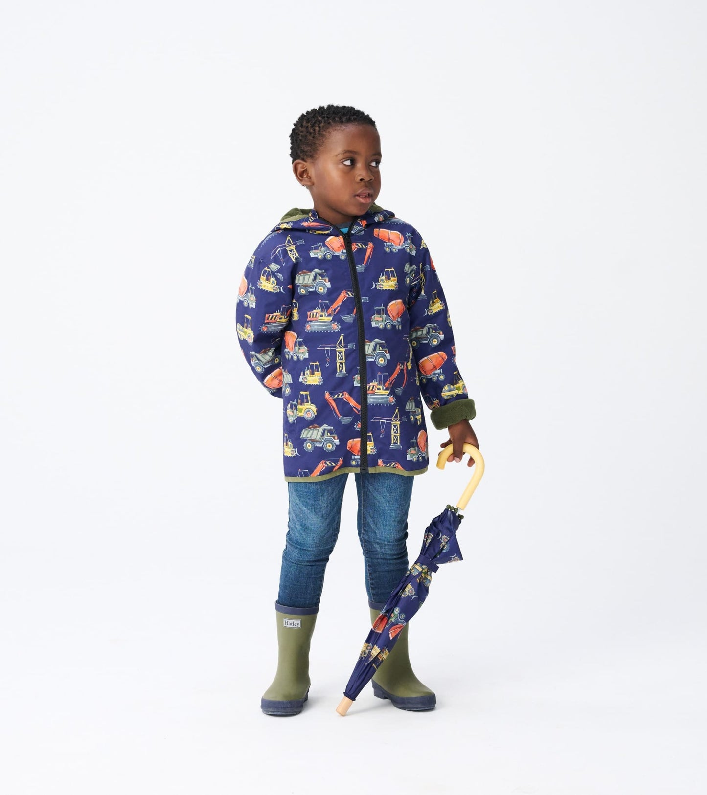 Navy microfiber jacket with construction truck print, hood, and green trim, worn by a child holding an umbrella.