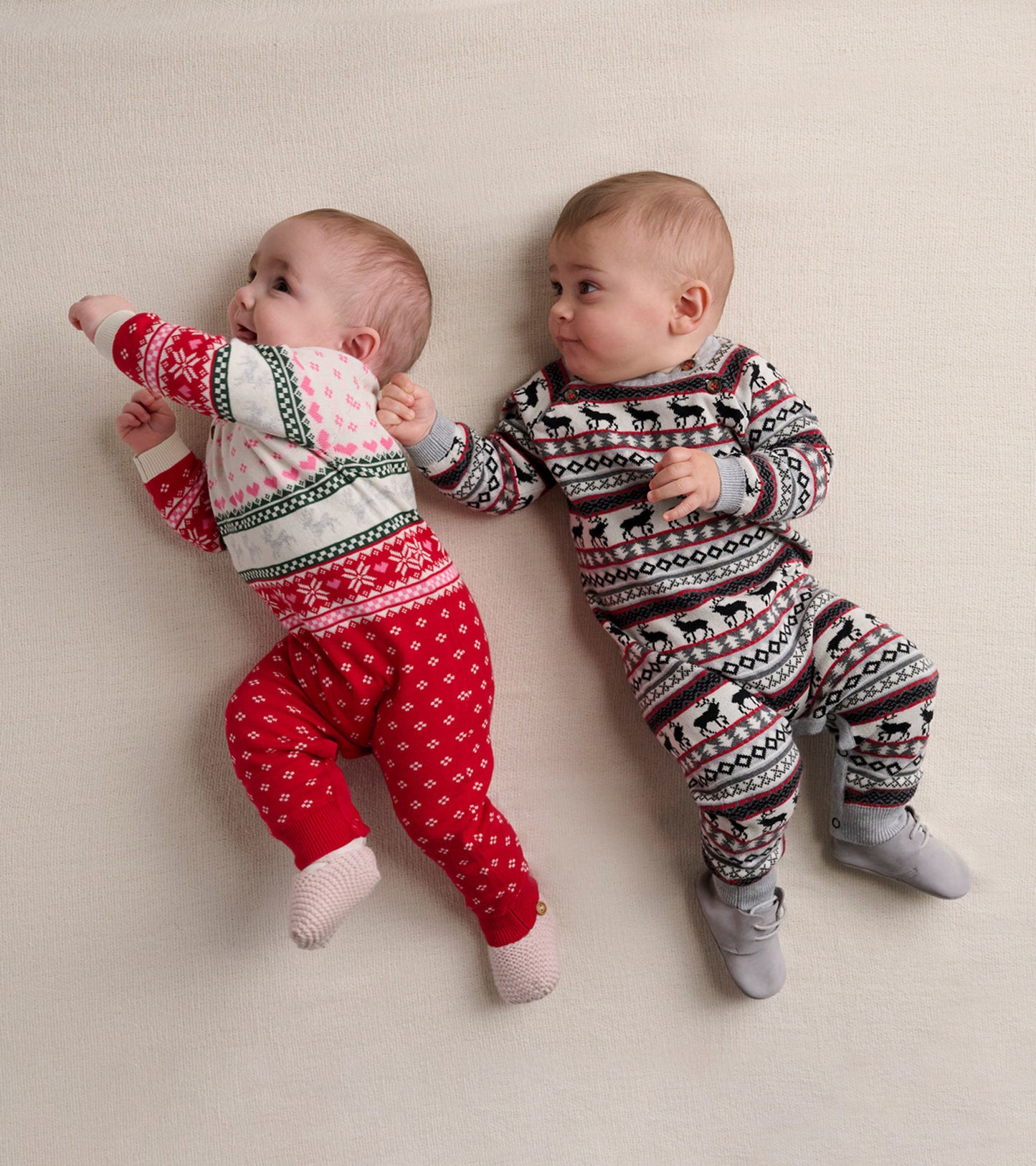 Two babies wearing colorful Fairisle pattern onesies, one in red and white, the other in black and grey, on a light backgrou…