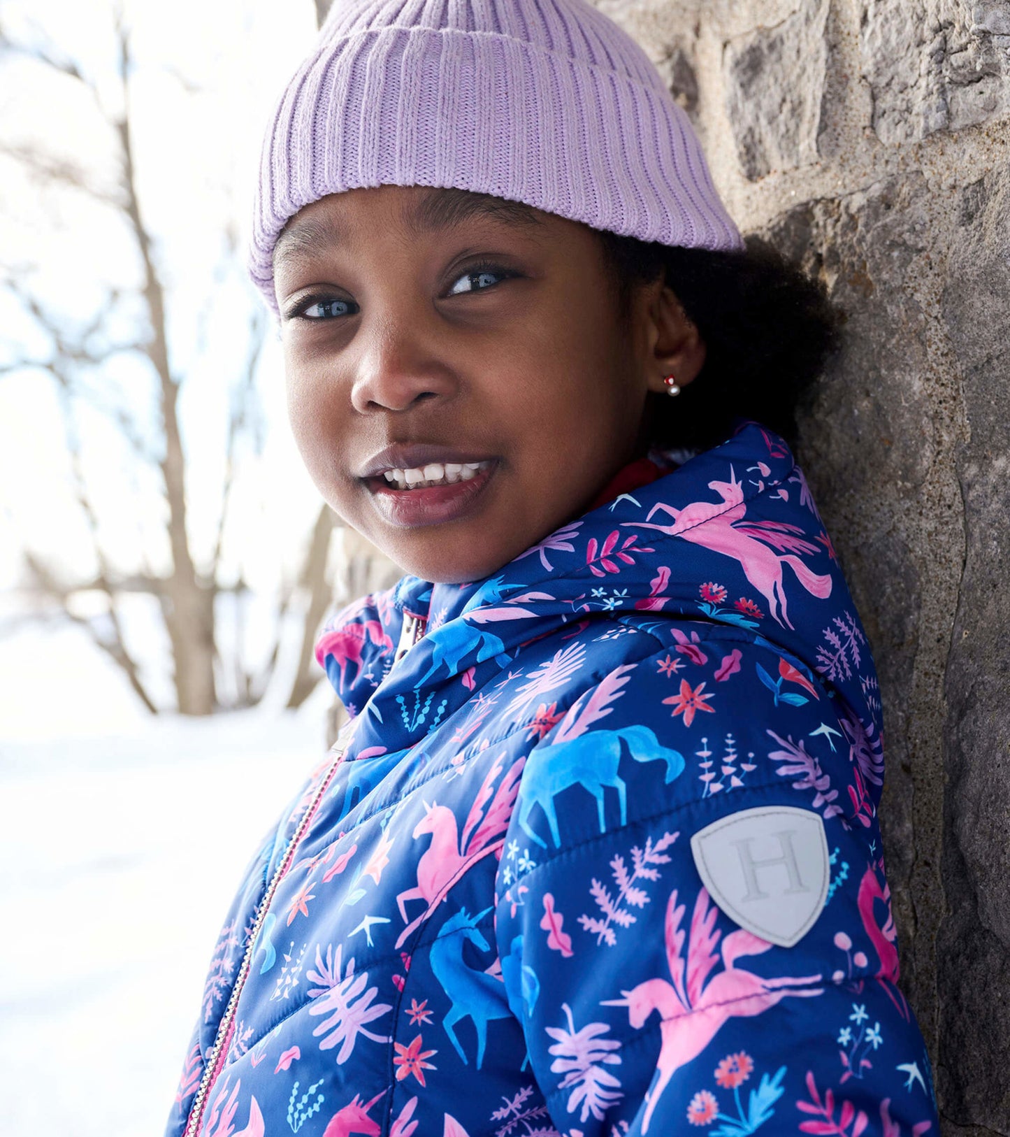 Blue puffer jacket with colorful unicorn and floral patterns, featuring a hood and zip closure, worn by a child outdoors.