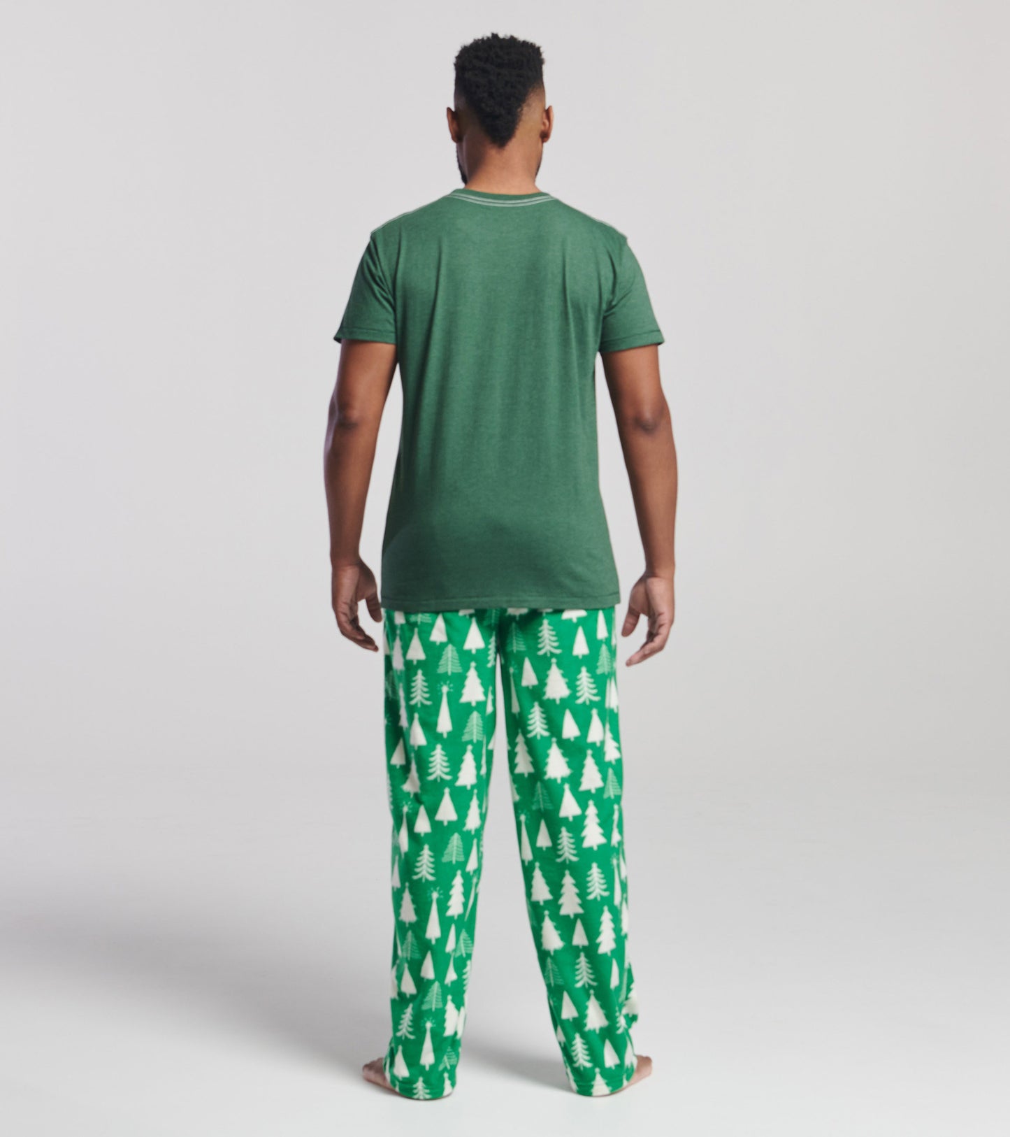 Green short-sleeve t-shirt worn with festive green pajama pants featuring white Christmas tree patterns, viewed from the bac…