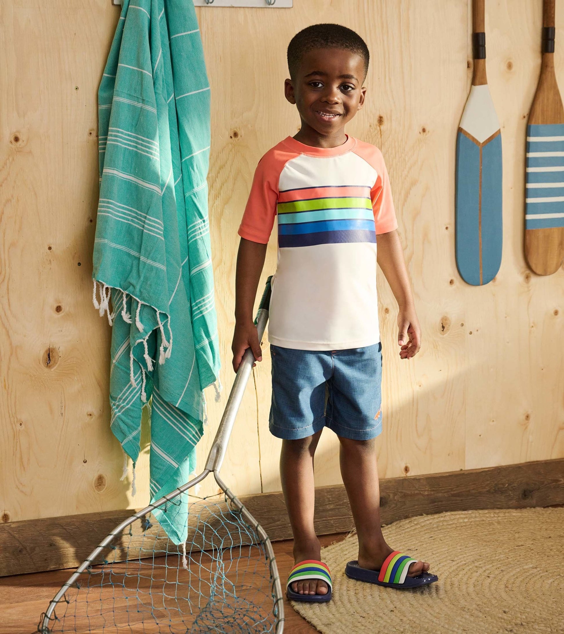 Short sleeve rashguard featuring a white body with colorful horizontal stripes and coral sleeves, worn by a smiling boy.