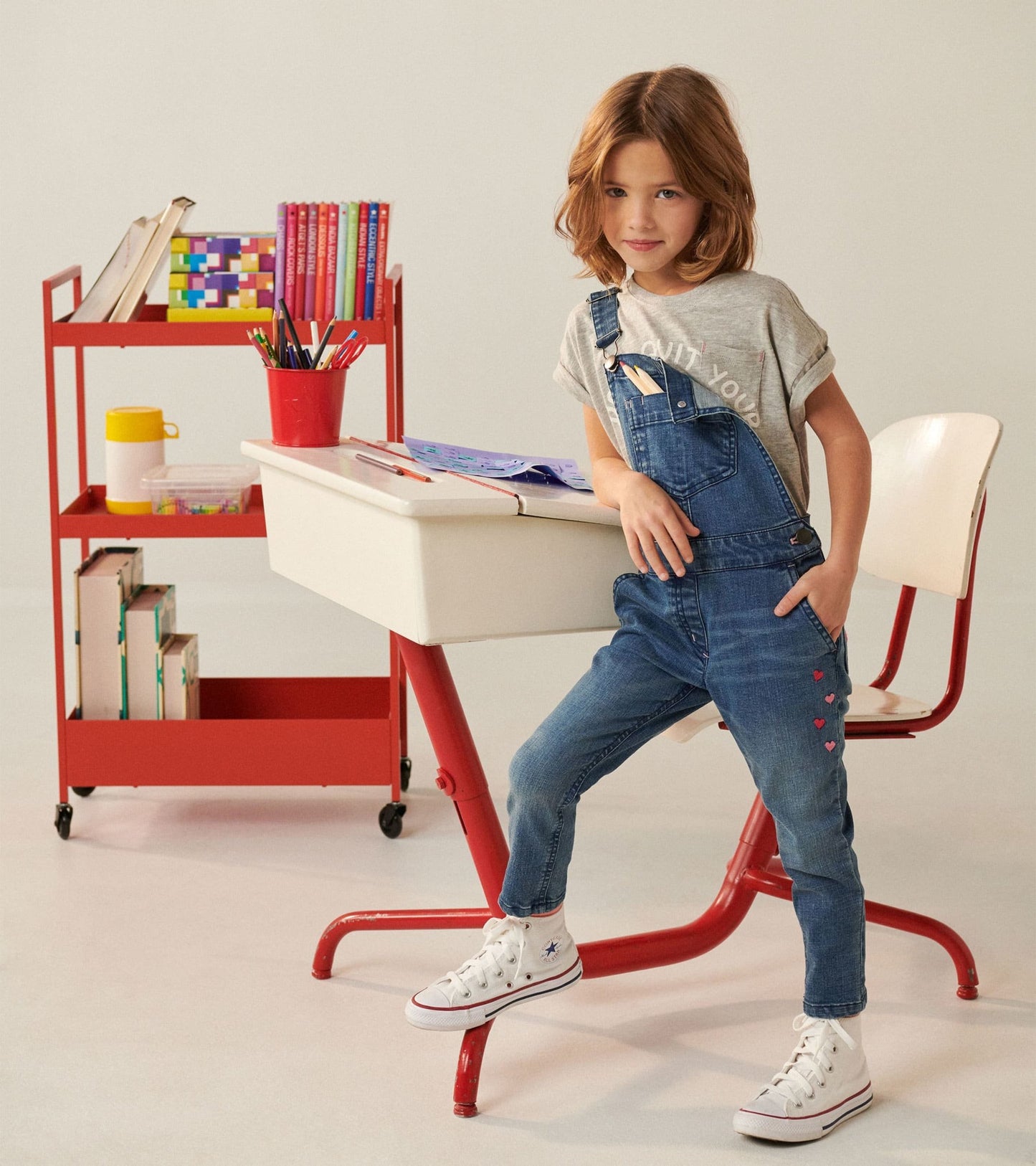 Denim stretch overalls in blue with heart details, styled with a gray shirt and white sneakers, perfect for casual wear.