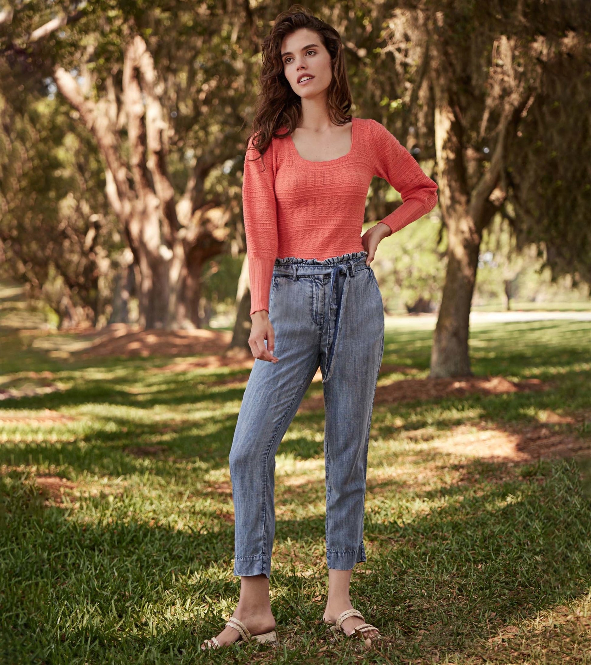 Blue acid rinse paper bag pants with a relaxed fit and drawstring waist, styled with a coral top in a natural setting.