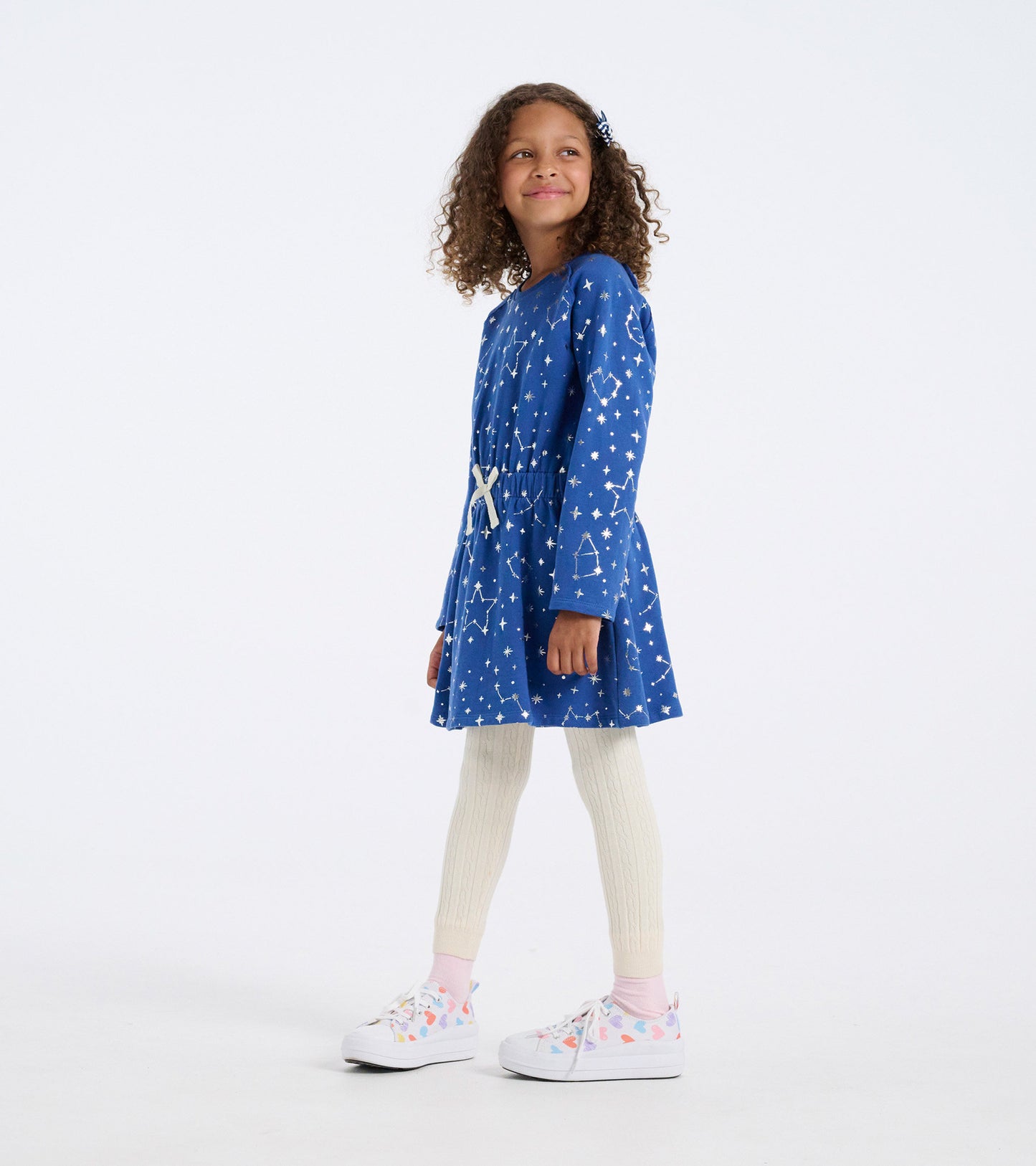 Blue terry dress with constellation pattern, gathered waist, long sleeves, paired with cream leggings and colorful sneakers.