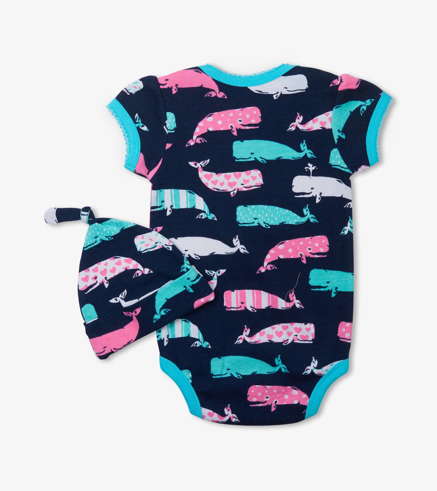 Pink and teal whale-patterned bodysuit with short sleeves and matching hat, set against a navy background.