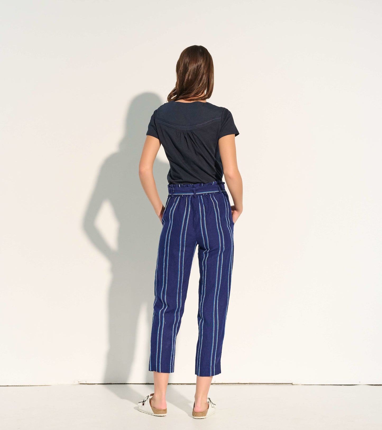 Navy paper bag pants with white and blue stripes, featuring a belted waist and cropped length, viewed from the back.