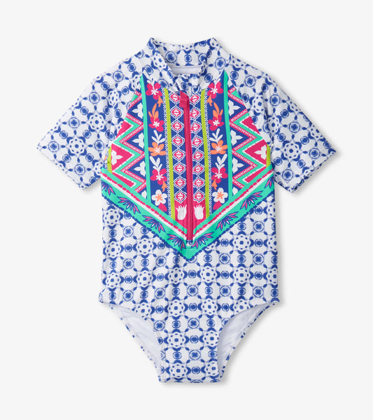 Short-sleeve one-piece rashguard featuring a colorful geometric pattern with floral accents on a blue background.