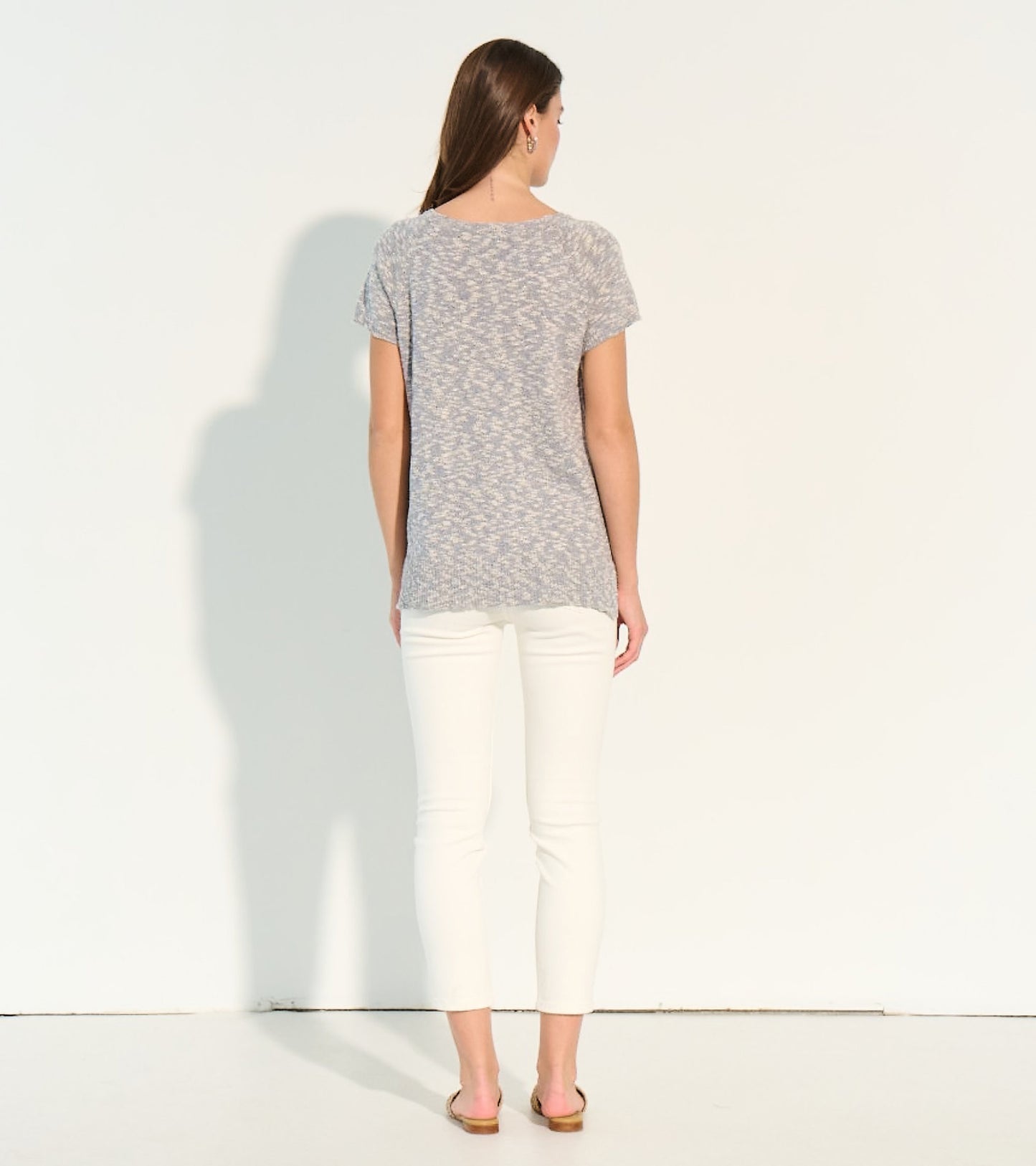 Back view of a lightweight, short-sleeve knit tee in a soft gray pattern, paired with white pants.