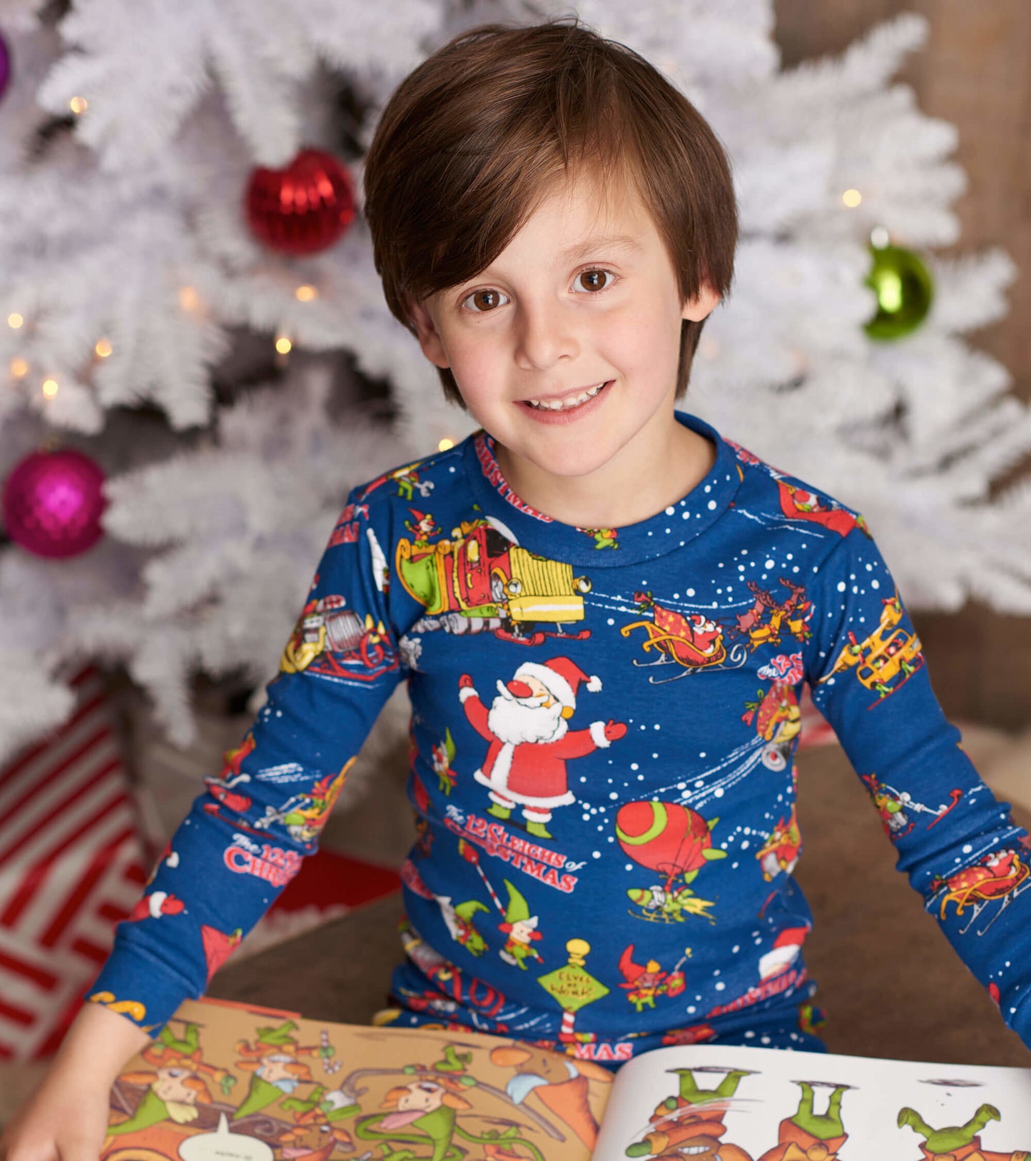 Blue long-sleeve pajama set featuring festive Christmas graphics, worn by a child sitting with a book.