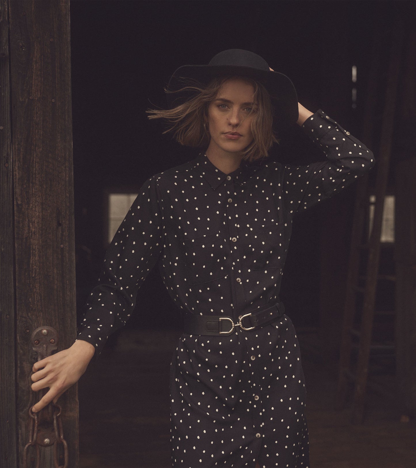 Black midi shirt dress with white polka dots, button-up front, and a belted waist, styled with a wide-brimmed hat.