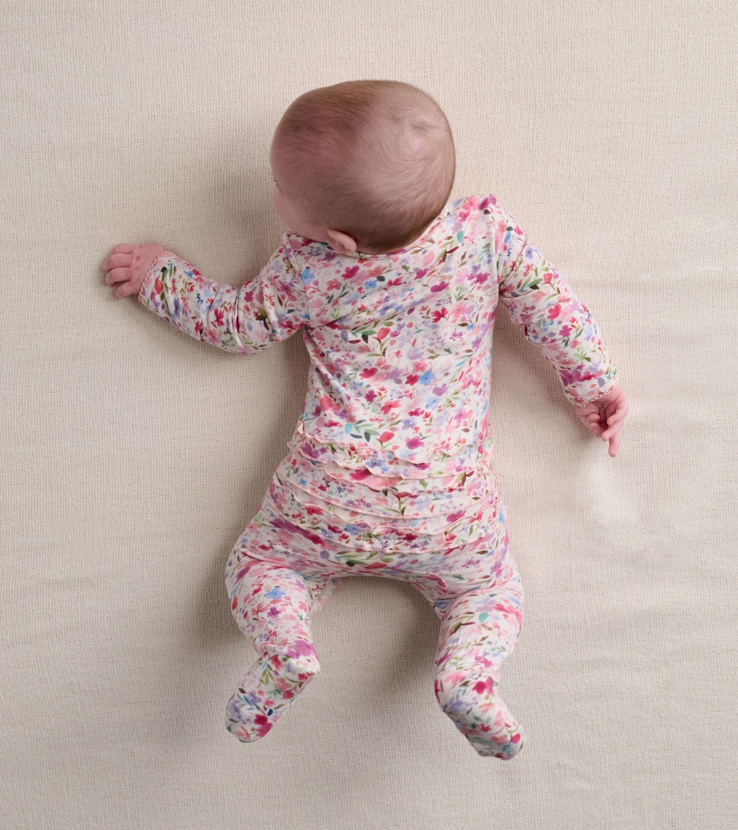 Floral-patterned footed sleeper in soft fabric, featuring ruffles on the bum, designed for babies up to 9 months.