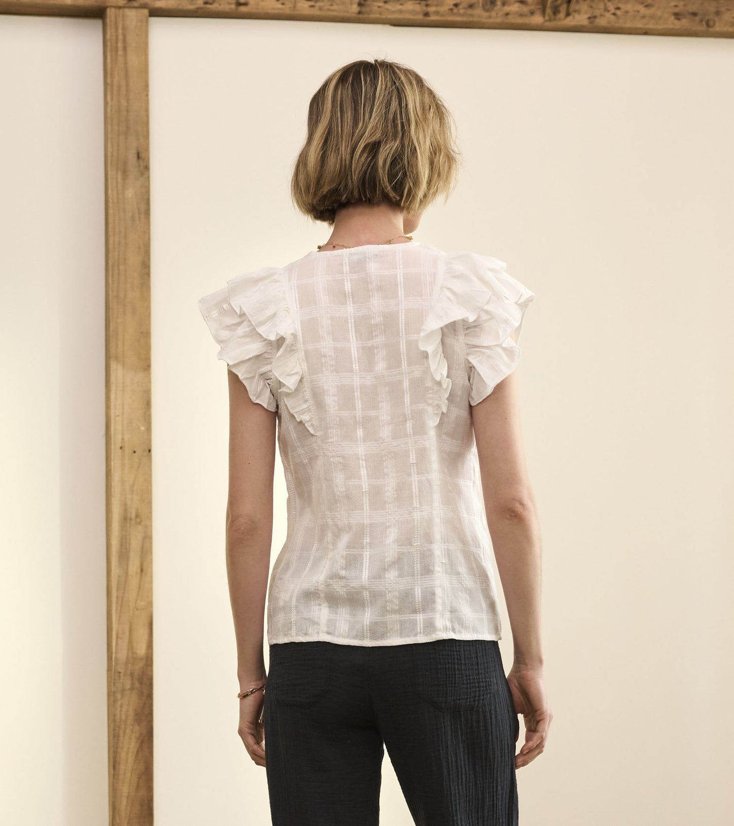White blouse with ruffled sleeves and a shadow plaid pattern, viewed from the back.