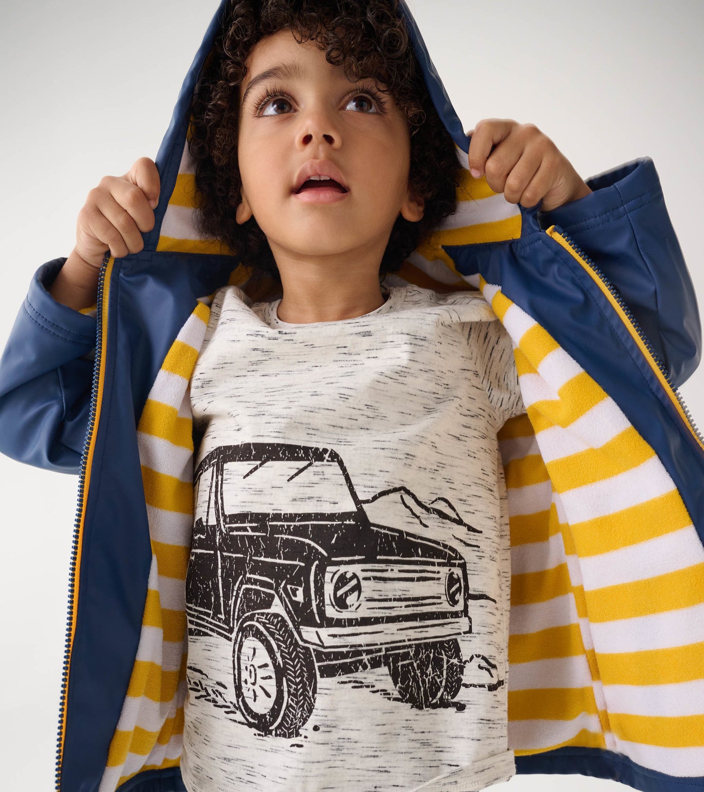 Navy zip-up rain jacket with a striped yellow and white lining, worn by a child holding the hood.