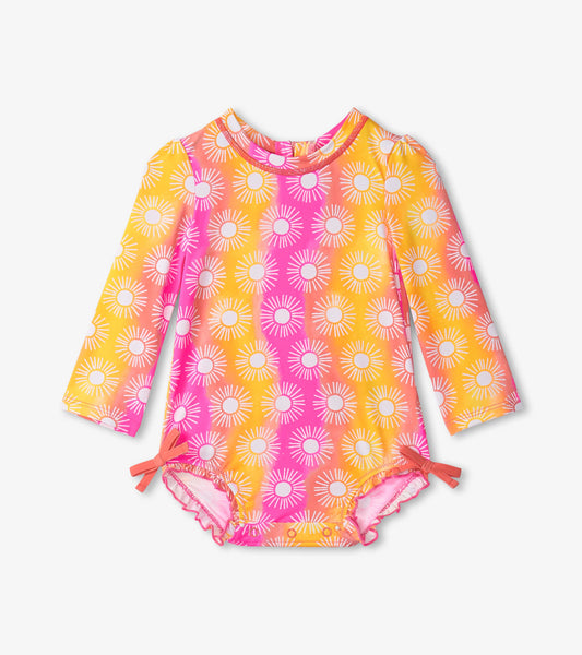 Long-sleeve baby swimsuit featuring a vibrant sun pattern in pink and yellow with side ties and ruffled edges.