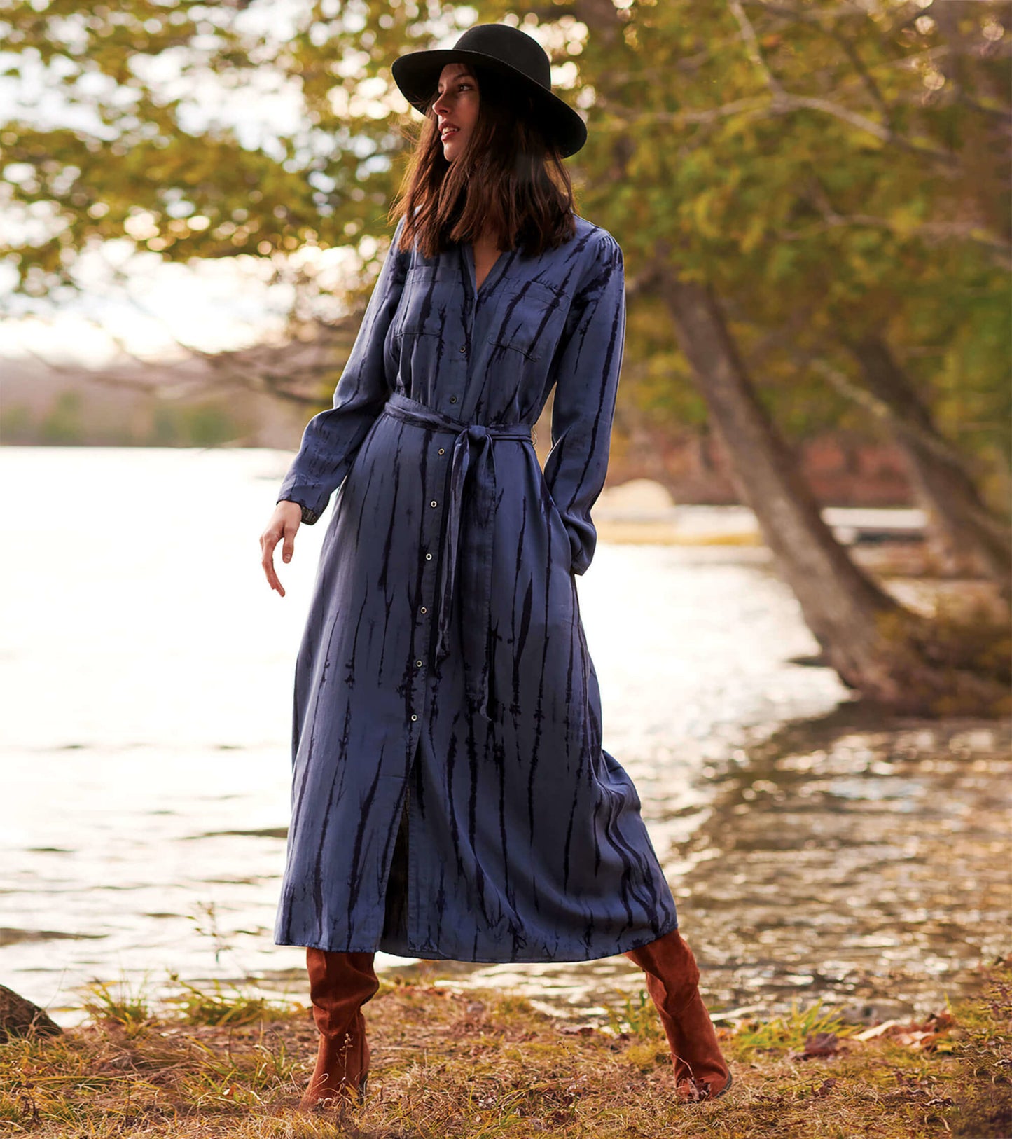 Long-sleeve maxi shirt dress in deep blue with a tie waist and vertical stripes, styled with a wide-brimmed hat and boots.