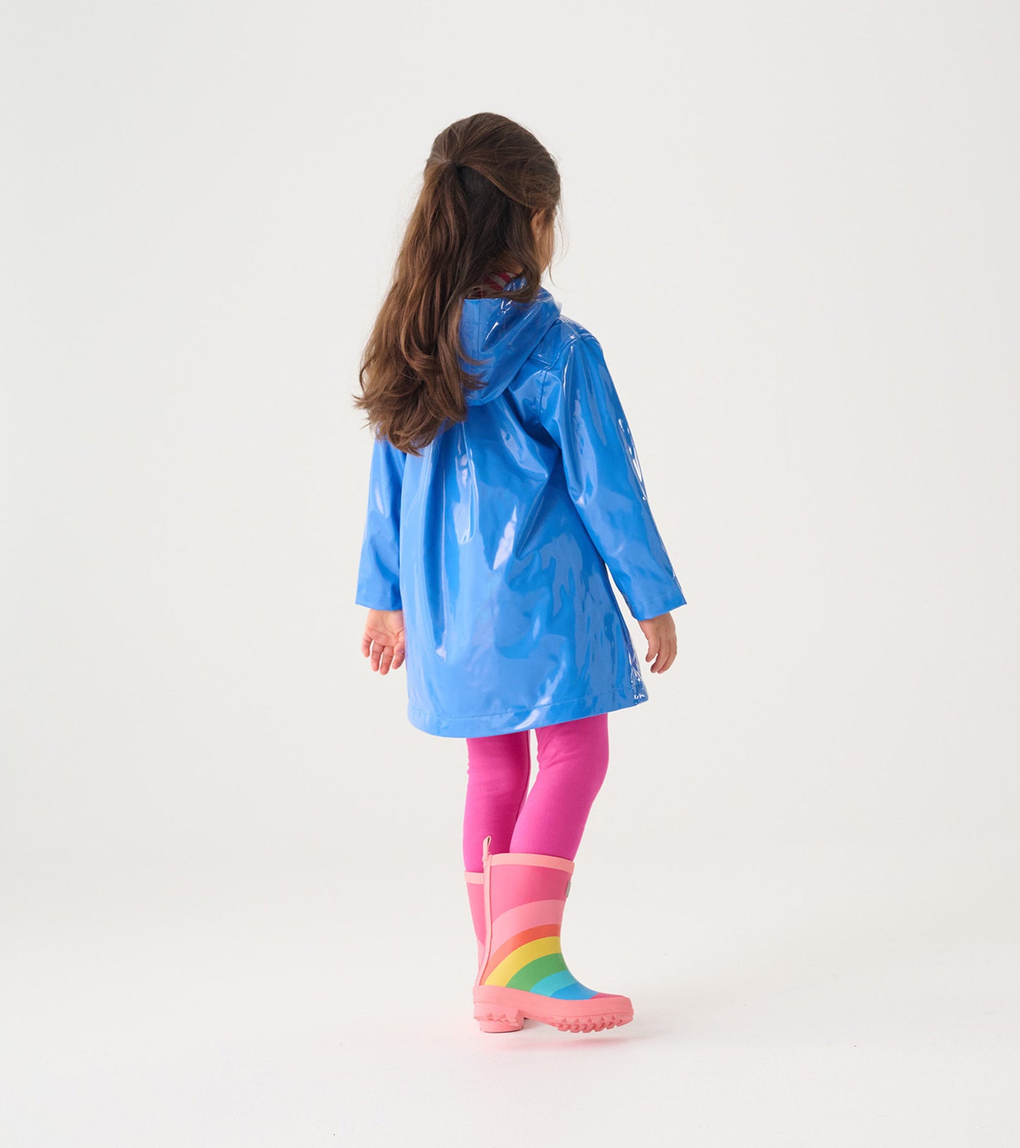 Blue glitter swing jacket with a hood, worn over pink leggings and rainbow rain boots, viewed from the back.