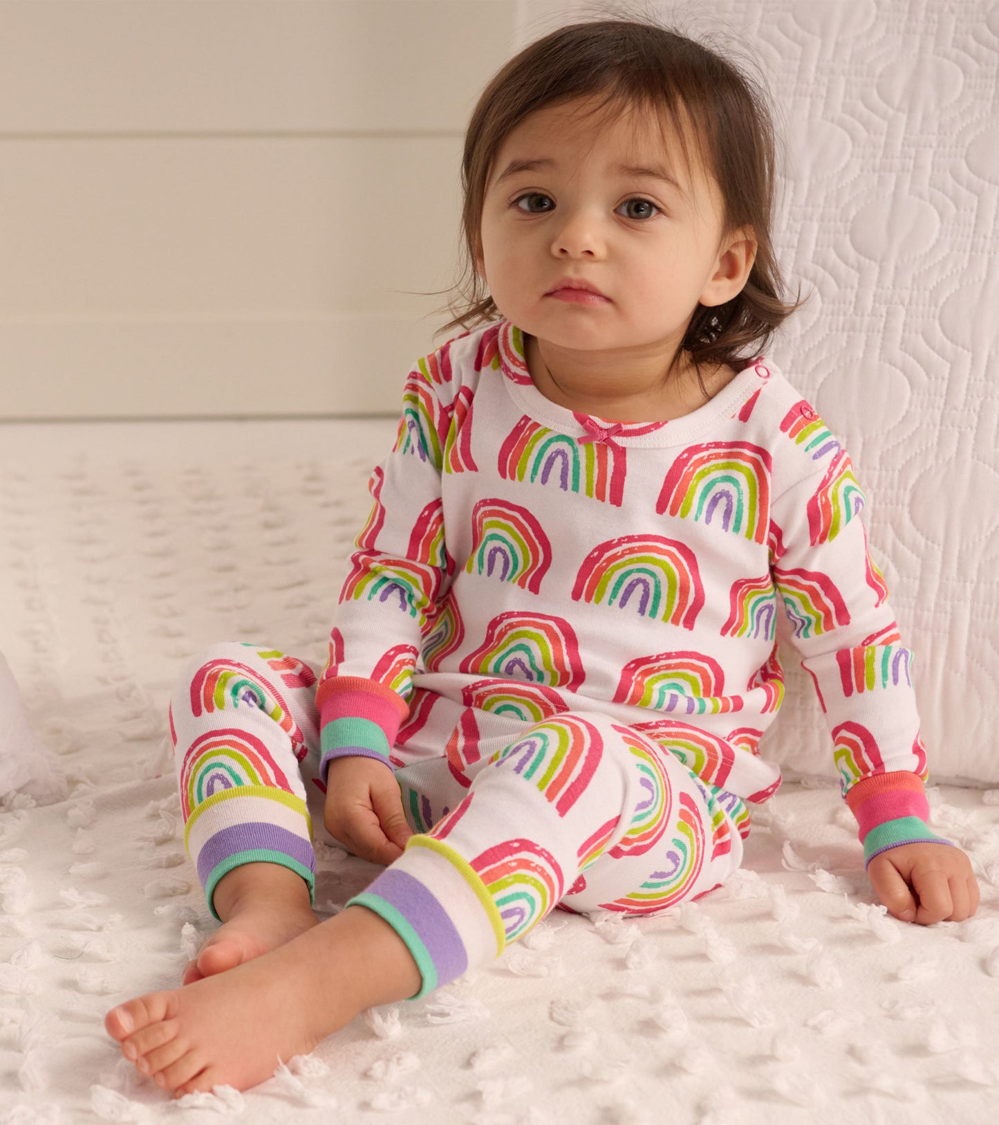 Organic cotton baby pajama set featuring colorful rainbow patterns, with contrasting cuffs and a relaxed fit.