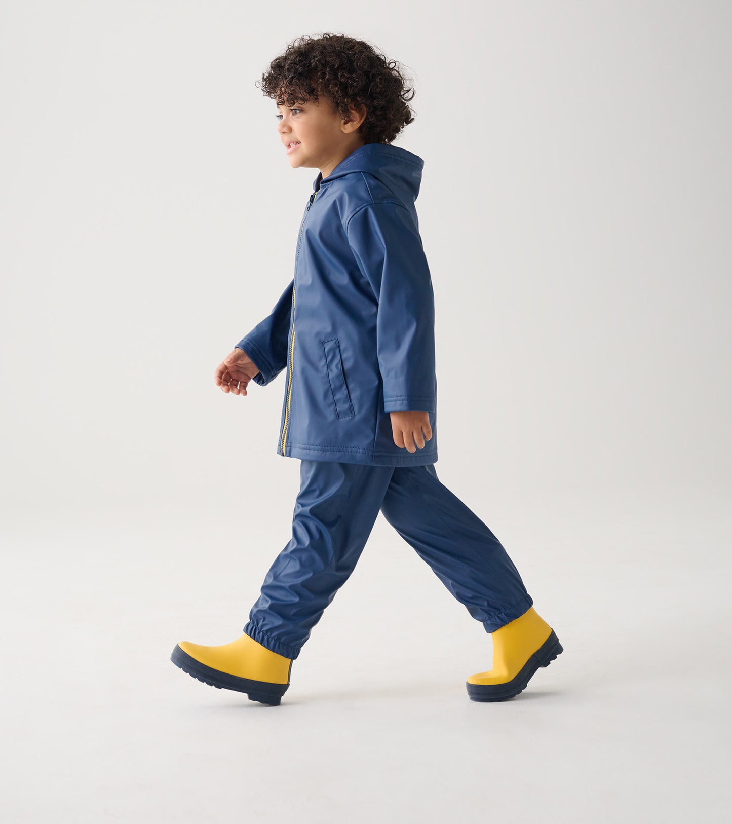 Navy zip-up rain jacket with hood, paired with matching pants and yellow rubber boots, worn by a child walking.