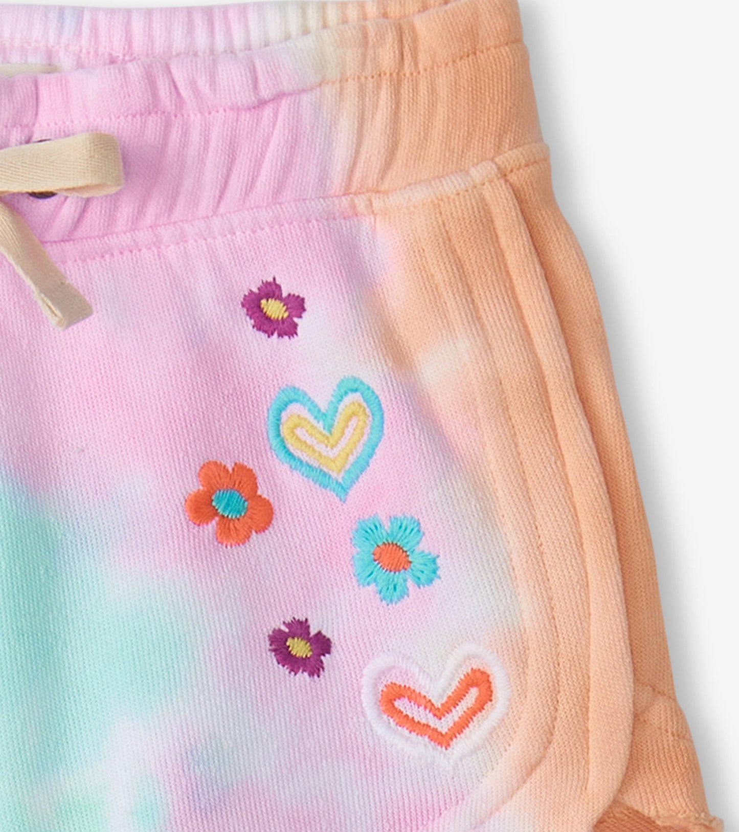 Pastel tie-dye pull-on shorts featuring colorful floral and heart embroidery. Elastic waistband with drawstring.