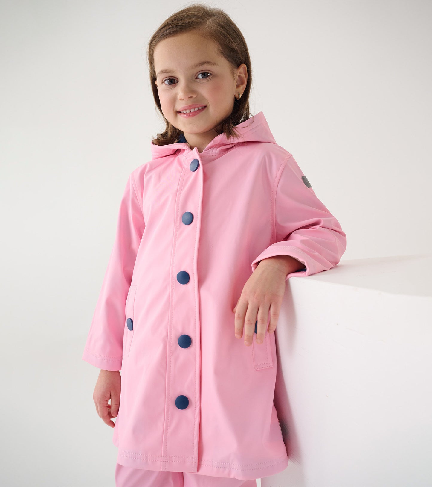 Pink button-up rain jacket with navy buttons and a hood, featuring a relaxed fit and side pockets.