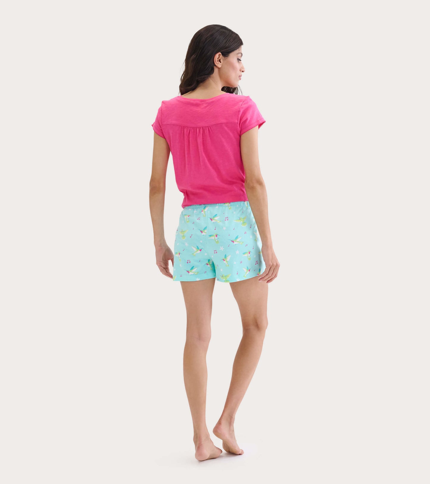 Pink V-neck tee with short sleeves, paired with light blue shorts featuring a colorful hummingbird pattern, viewed from the…