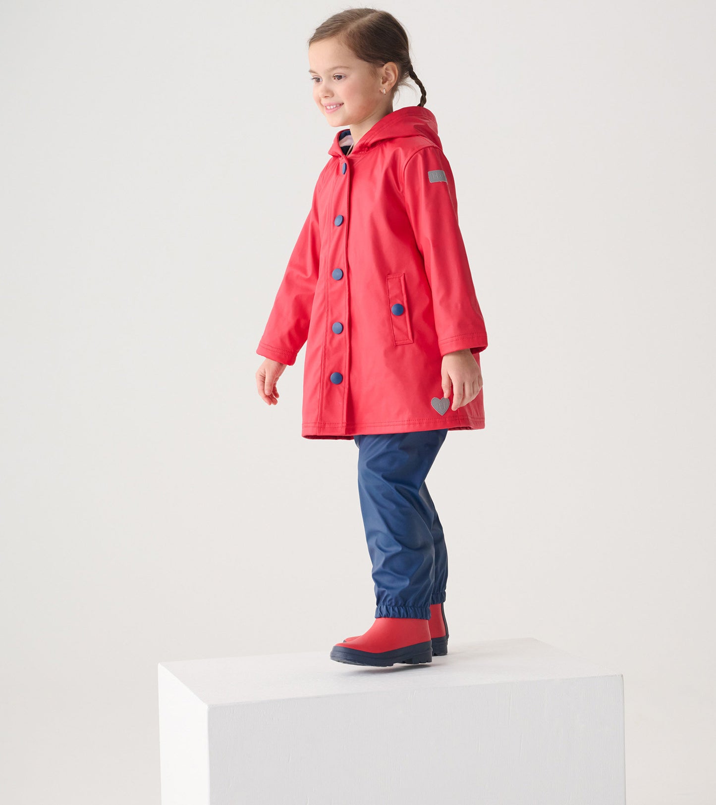 Red button-up rain jacket with a hood, featuring blue buttons, worn by a child standing on a pedestal.