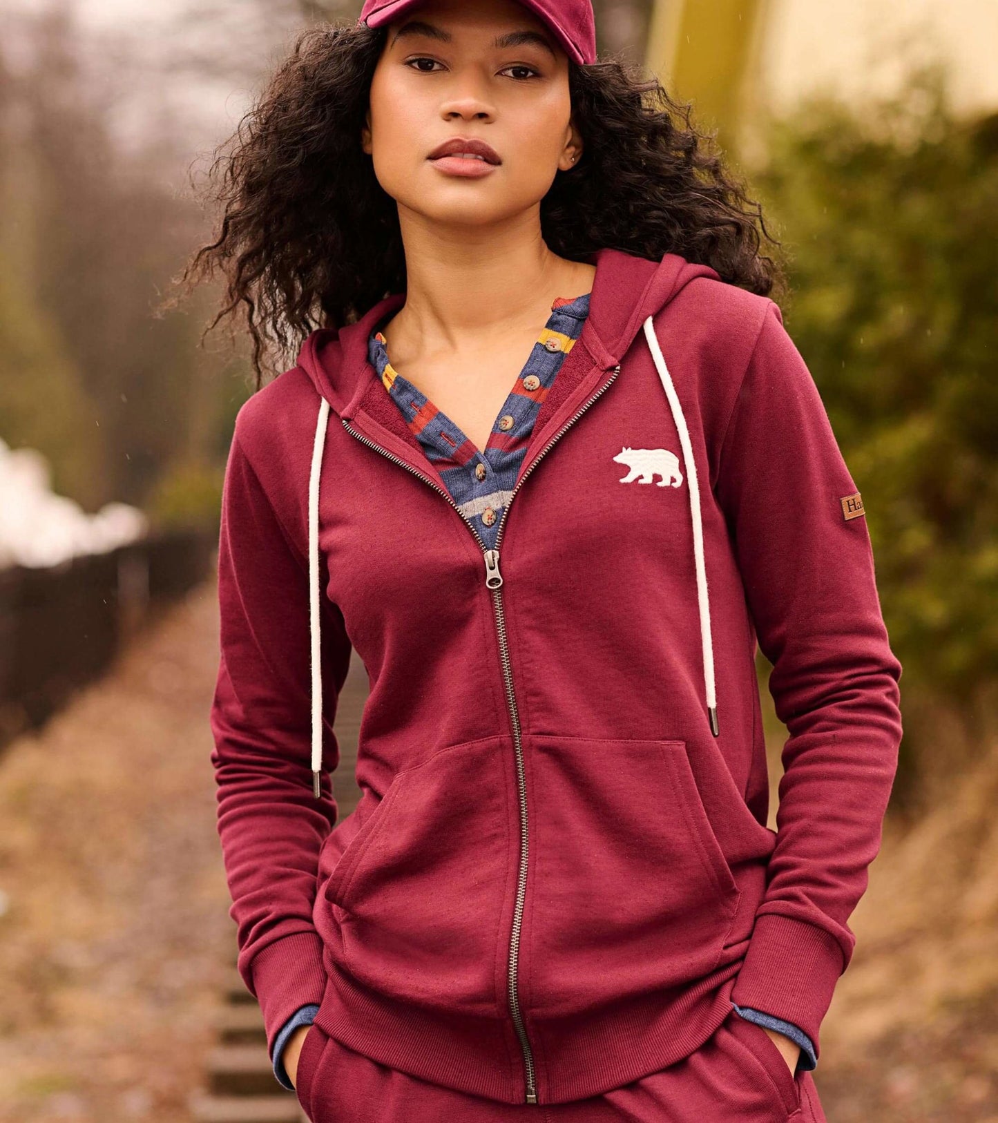Maroon full zip hoodie with bear graphic, drawstring hood, and front pockets, worn by a model outdoors.