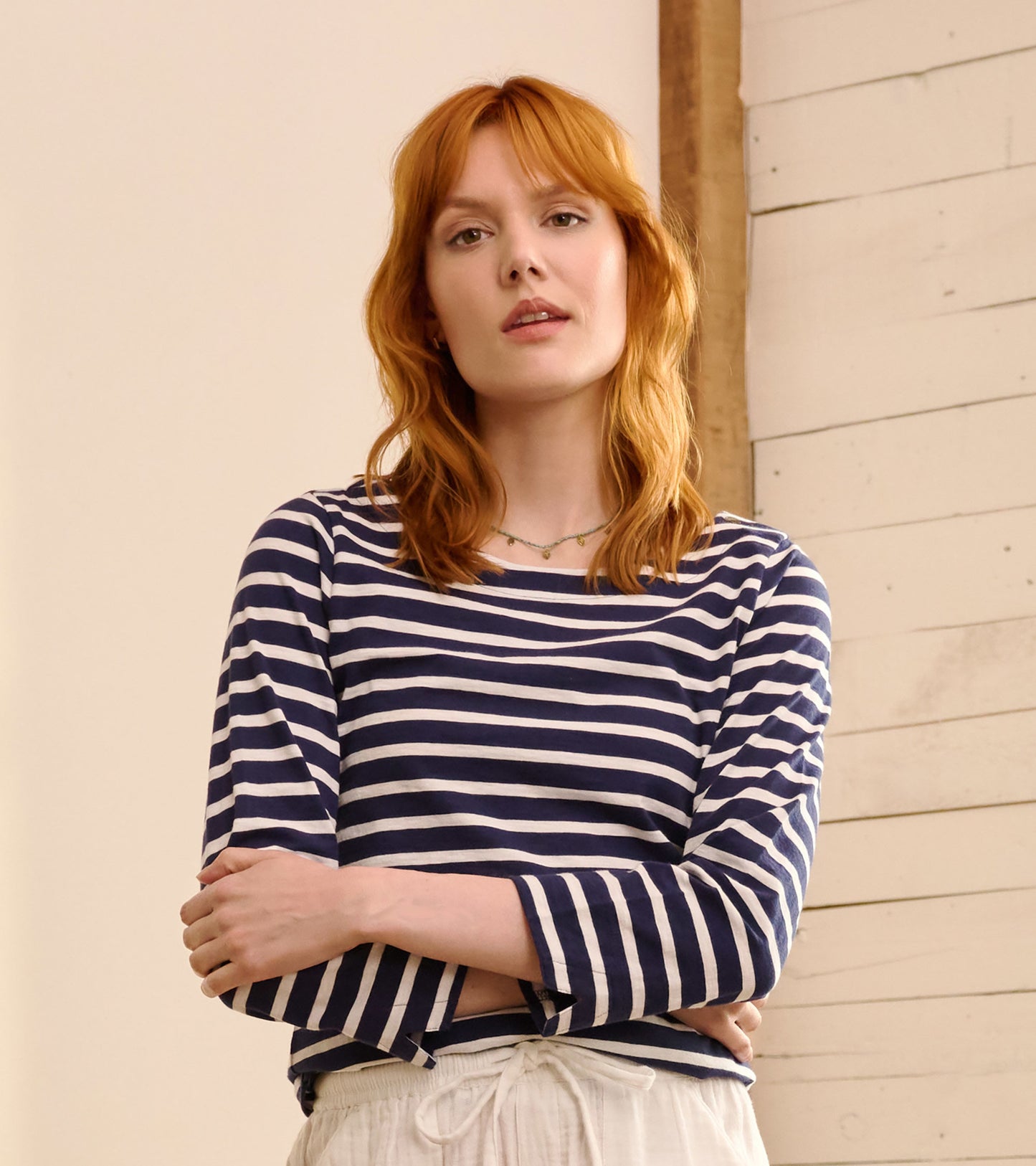 Navy blue striped long-sleeve top with a relaxed fit and boat neckline, styled with casual white pants.