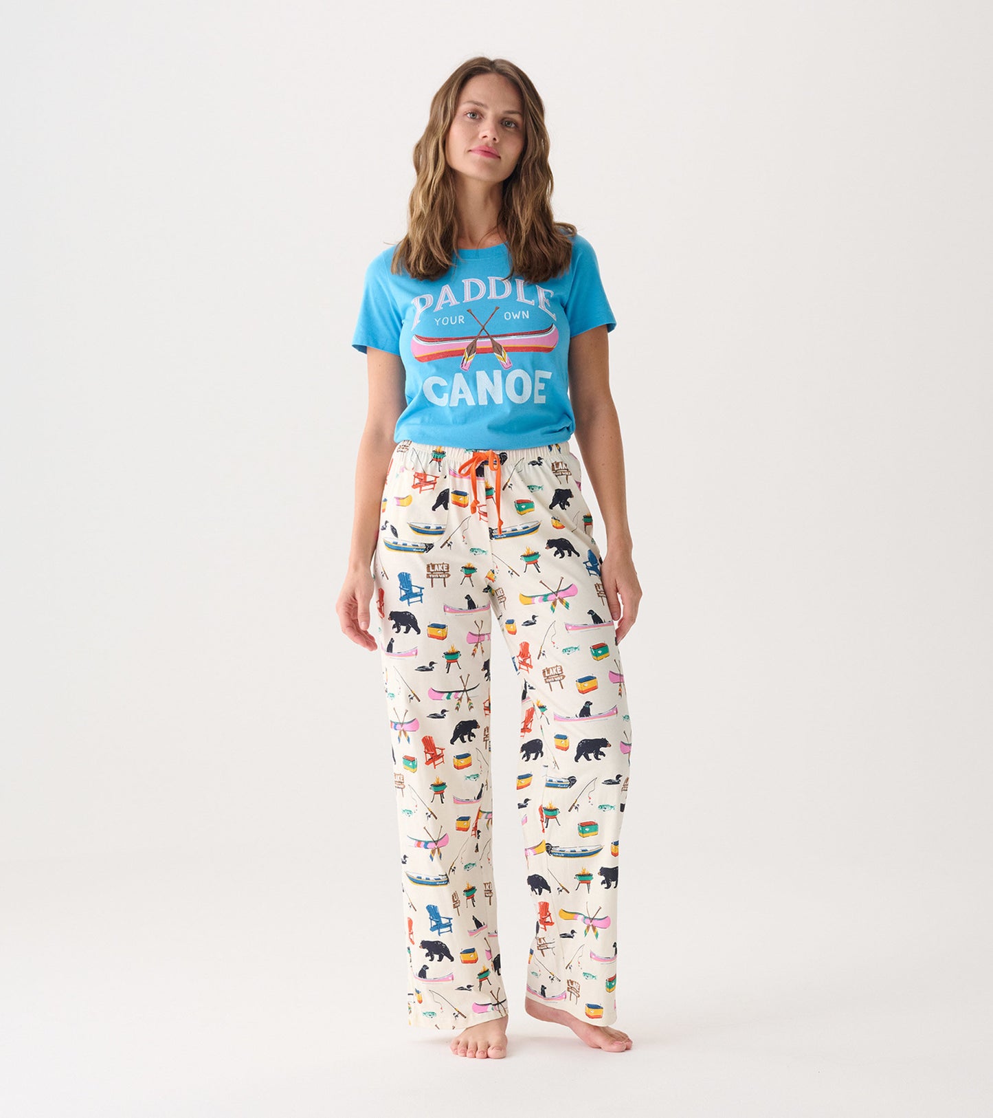 Women's cotton pajama pants in cream with colorful outdoor-themed prints and an adjustable orange drawstring waist.