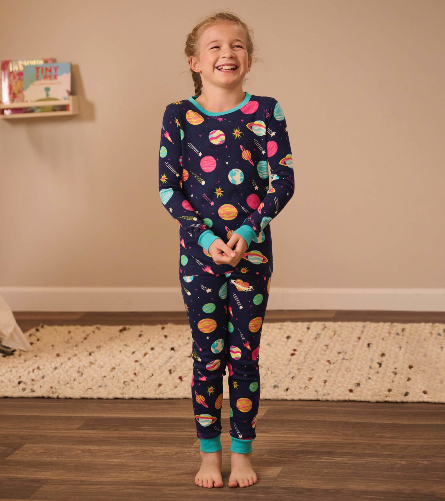 Navy organic cotton pajama set featuring colorful planets and stars, with turquoise cuffs and neckline, suitable for kids.
