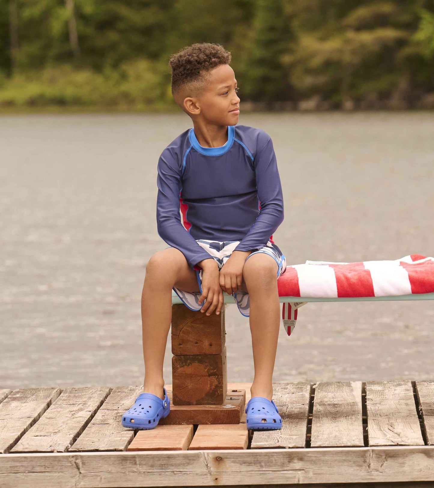 Nautical long sleeve rashguard in navy with colorblock accents, worn by a boy sitting on a dock by the water.