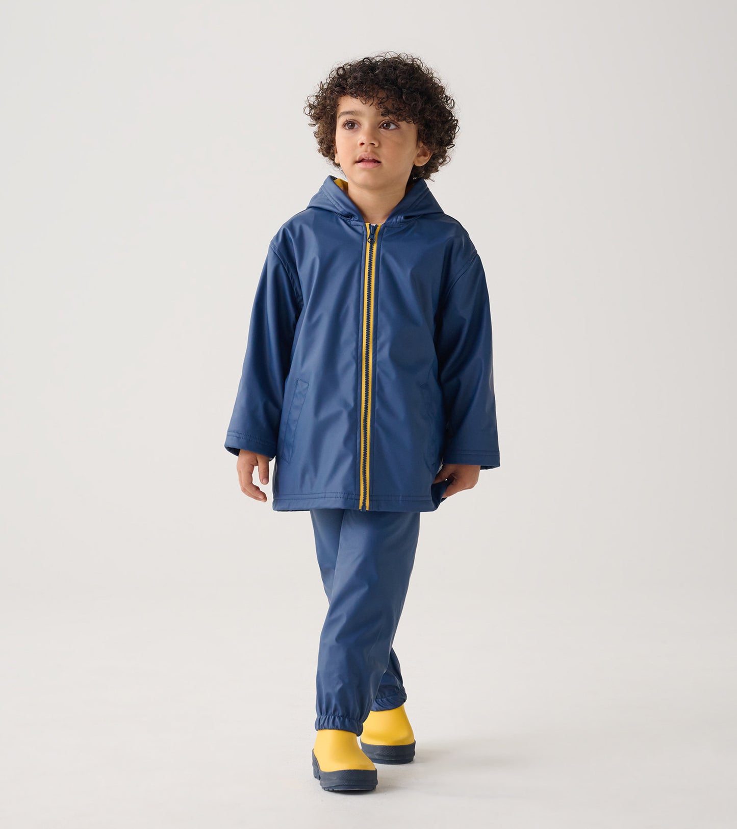 Navy zip-up rain jacket with a hood, featuring a yellow zipper, worn by a child with curly hair.