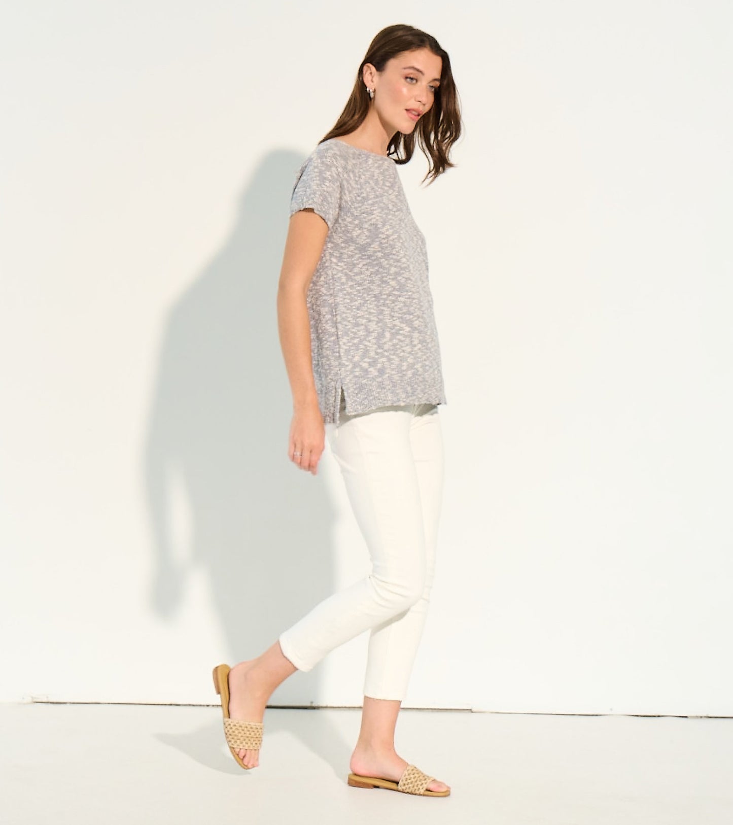 Light gray knit tee with short sleeves and side slits, paired with white pants and sandals, shown from the side.