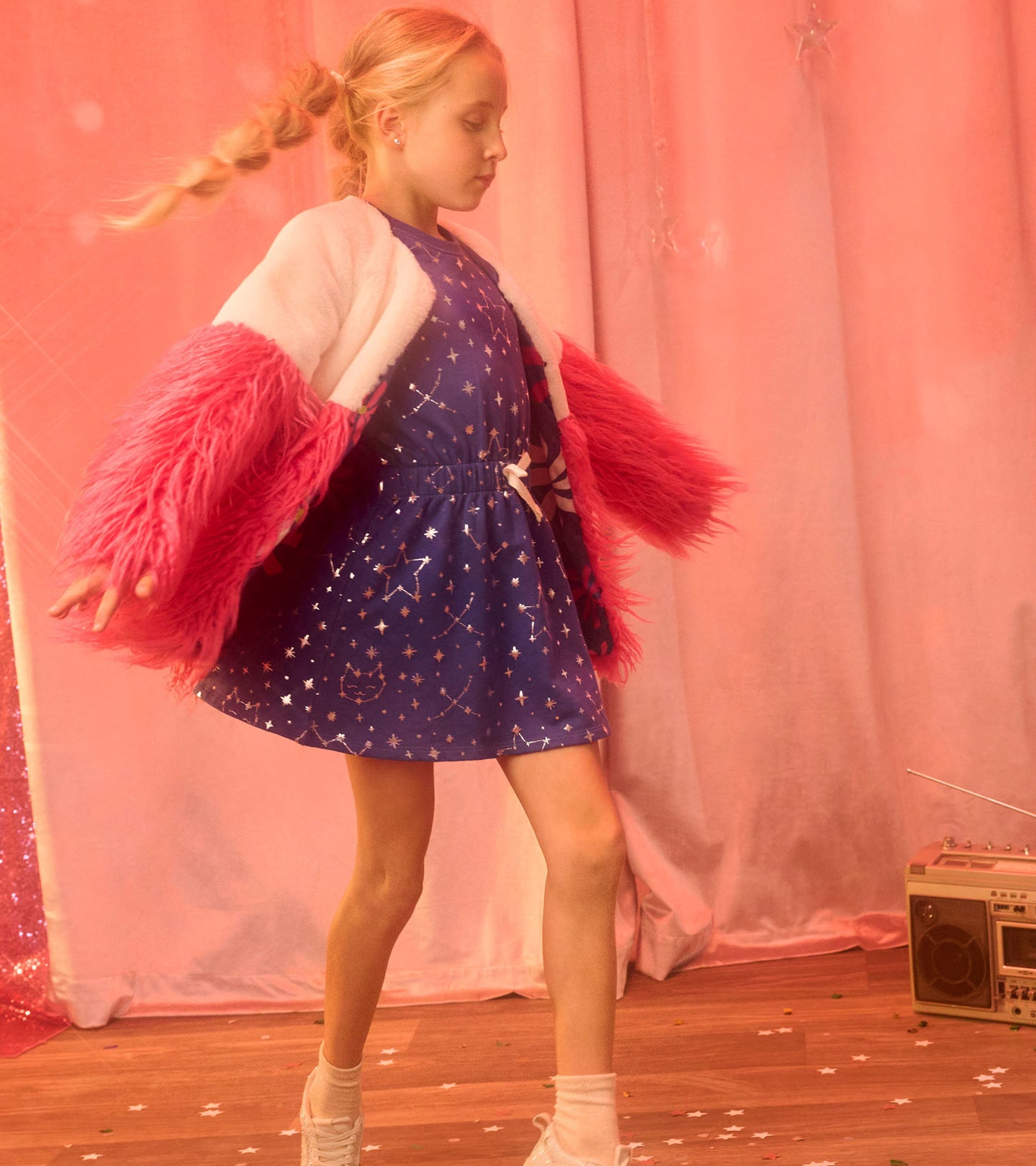 Blue terry dress with constellation pattern, cinched waist, and a pink fluffy cardigan, worn by a girl in motion.