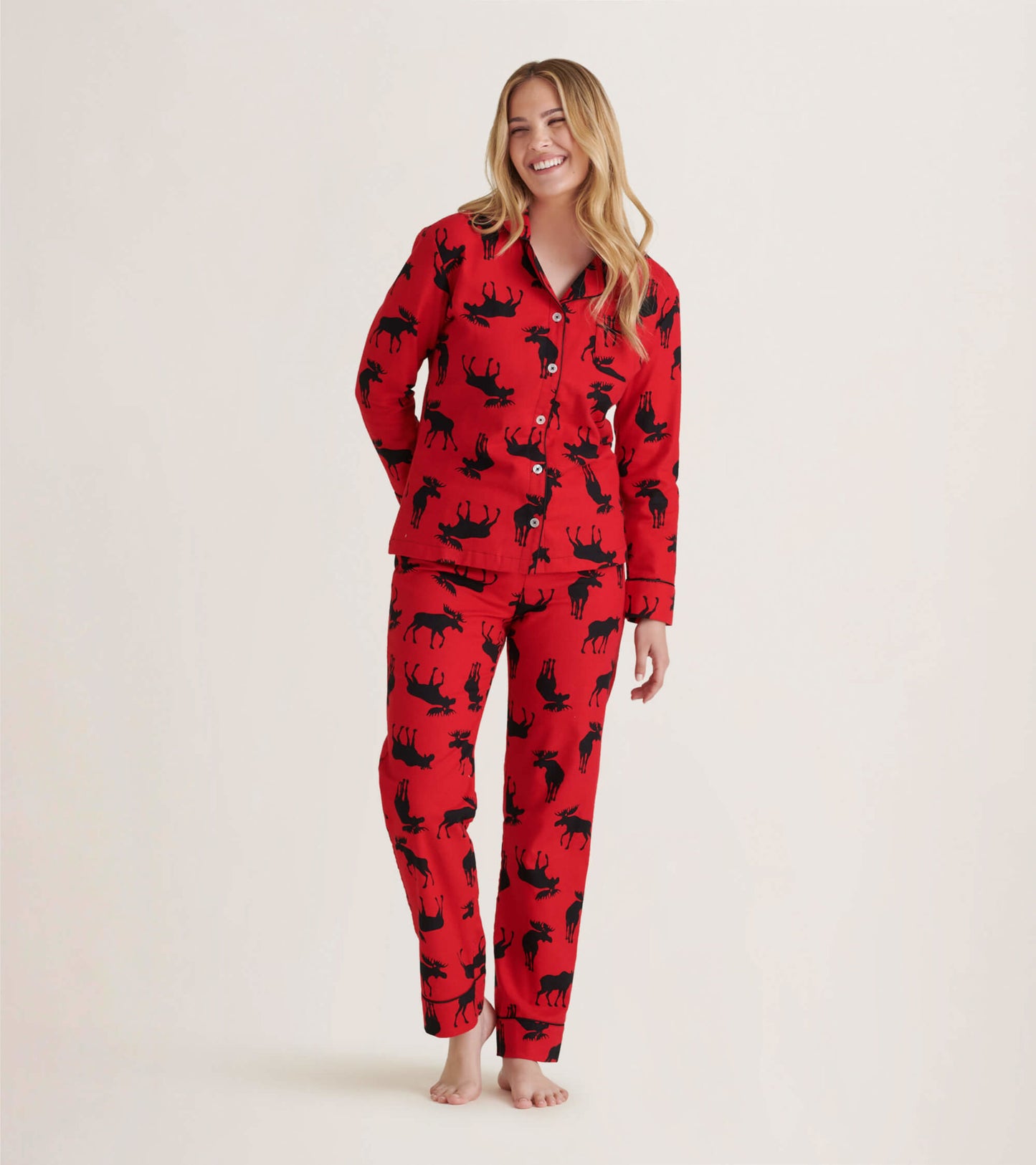 Red flannel pajama set featuring black moose patterns, includes button-up top and matching pants, worn by a smiling model.