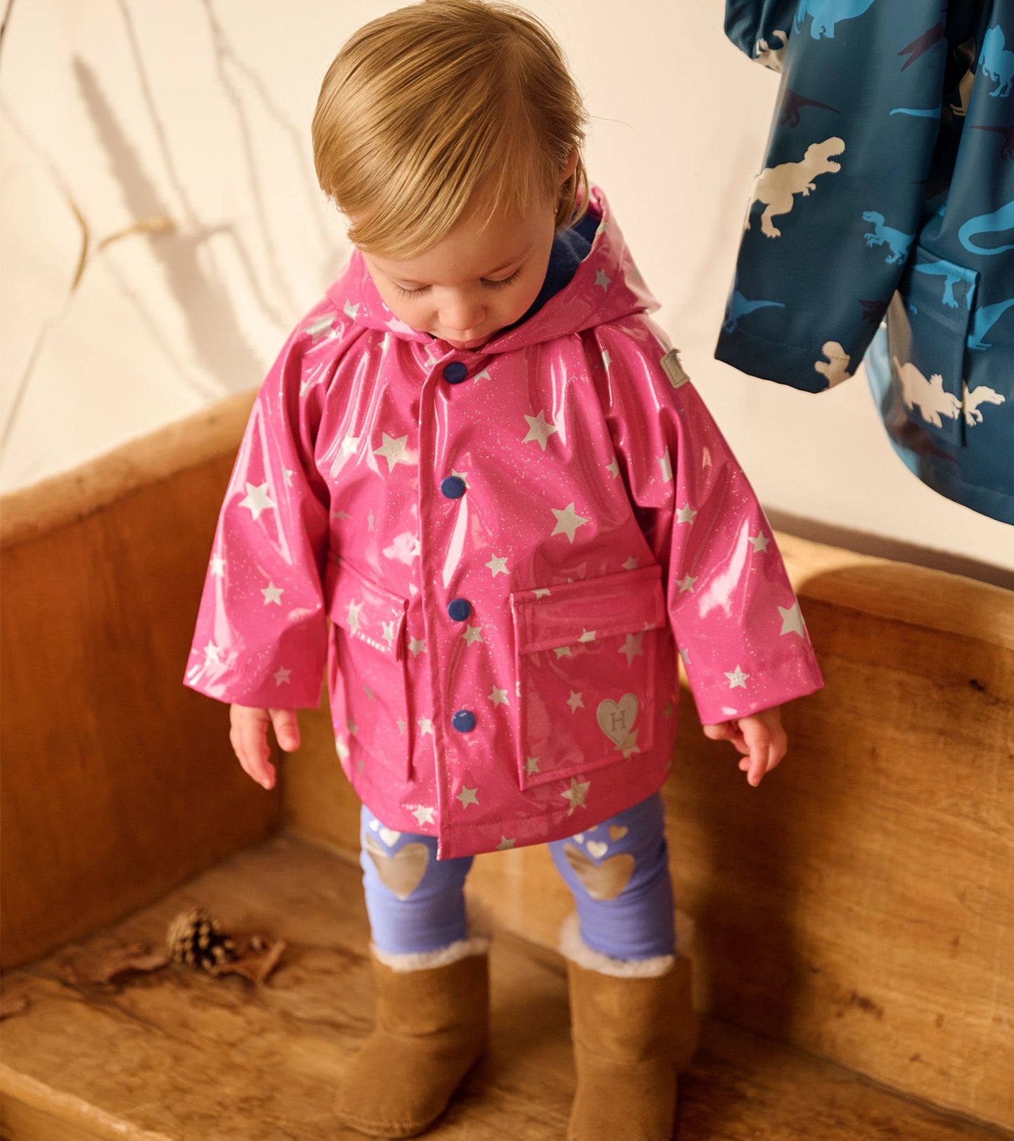 Pink glittery raincoat with star pattern, featuring a hood and blue buttons, worn by a child with brown boots.
