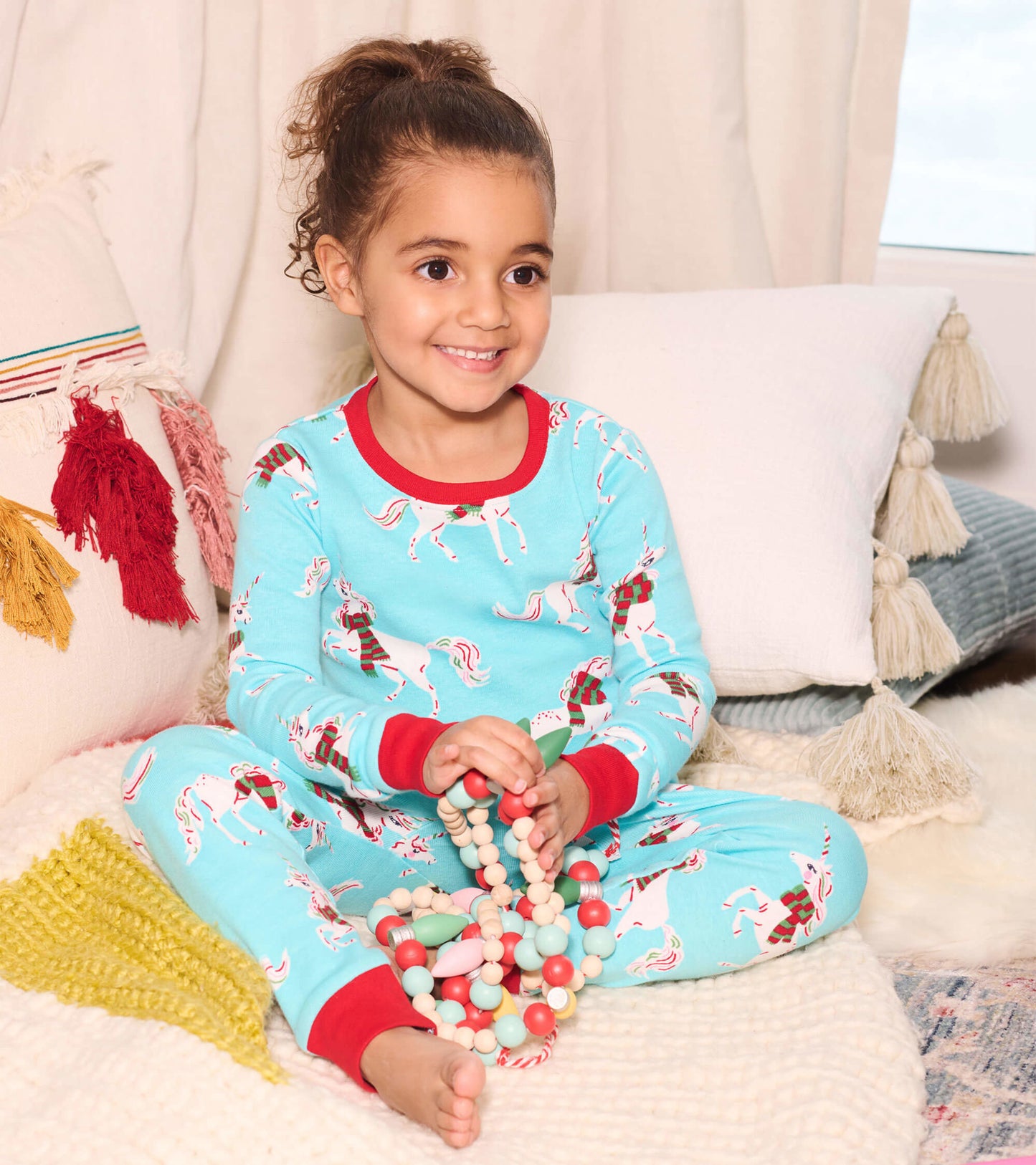 Light blue organic cotton pajama set featuring festive unicorns, red trim, and a playful design, worn by a smiling child.