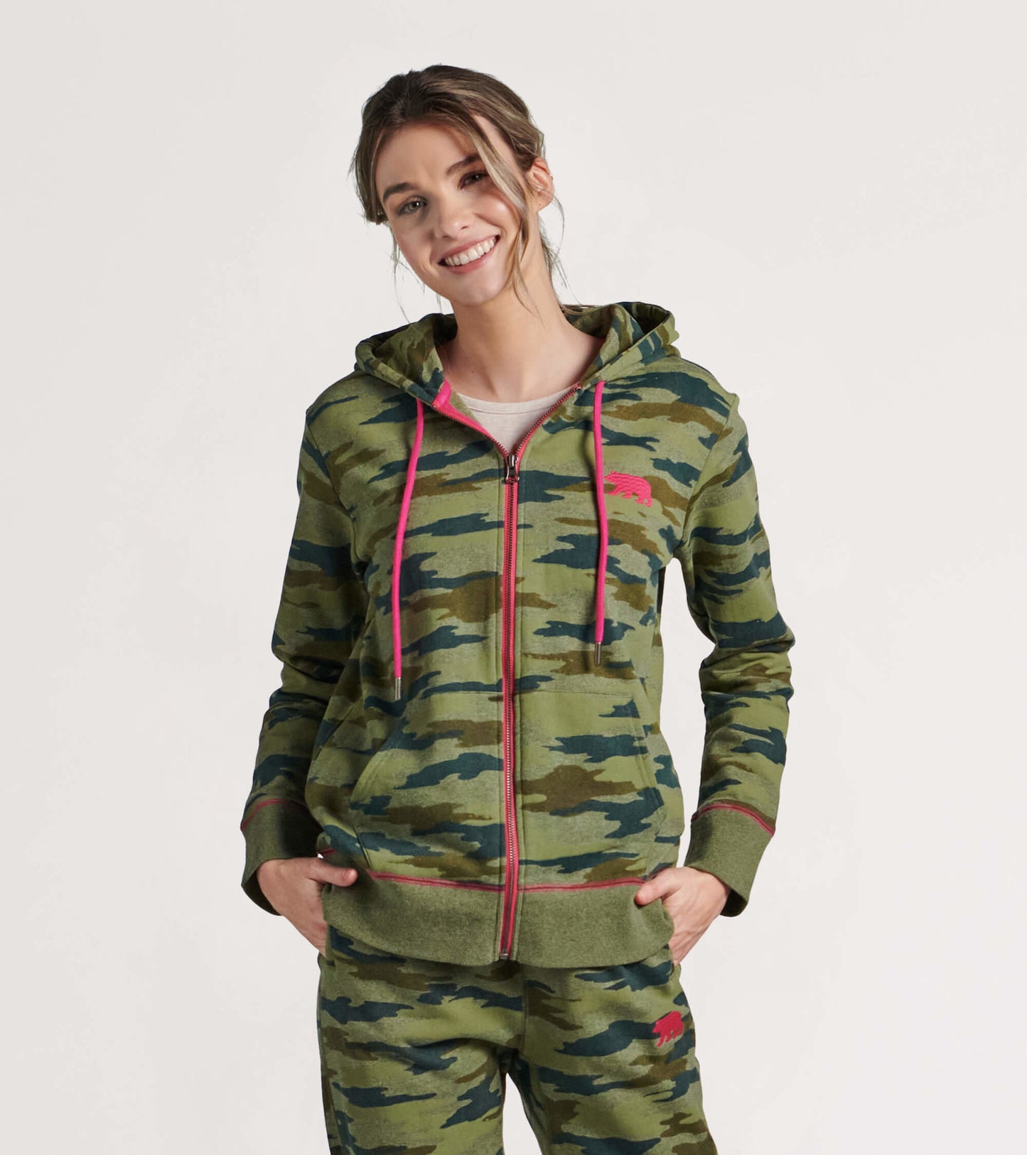 Green camouflage full zip hoodie with pink drawstrings, featuring a relaxed fit and front pockets.