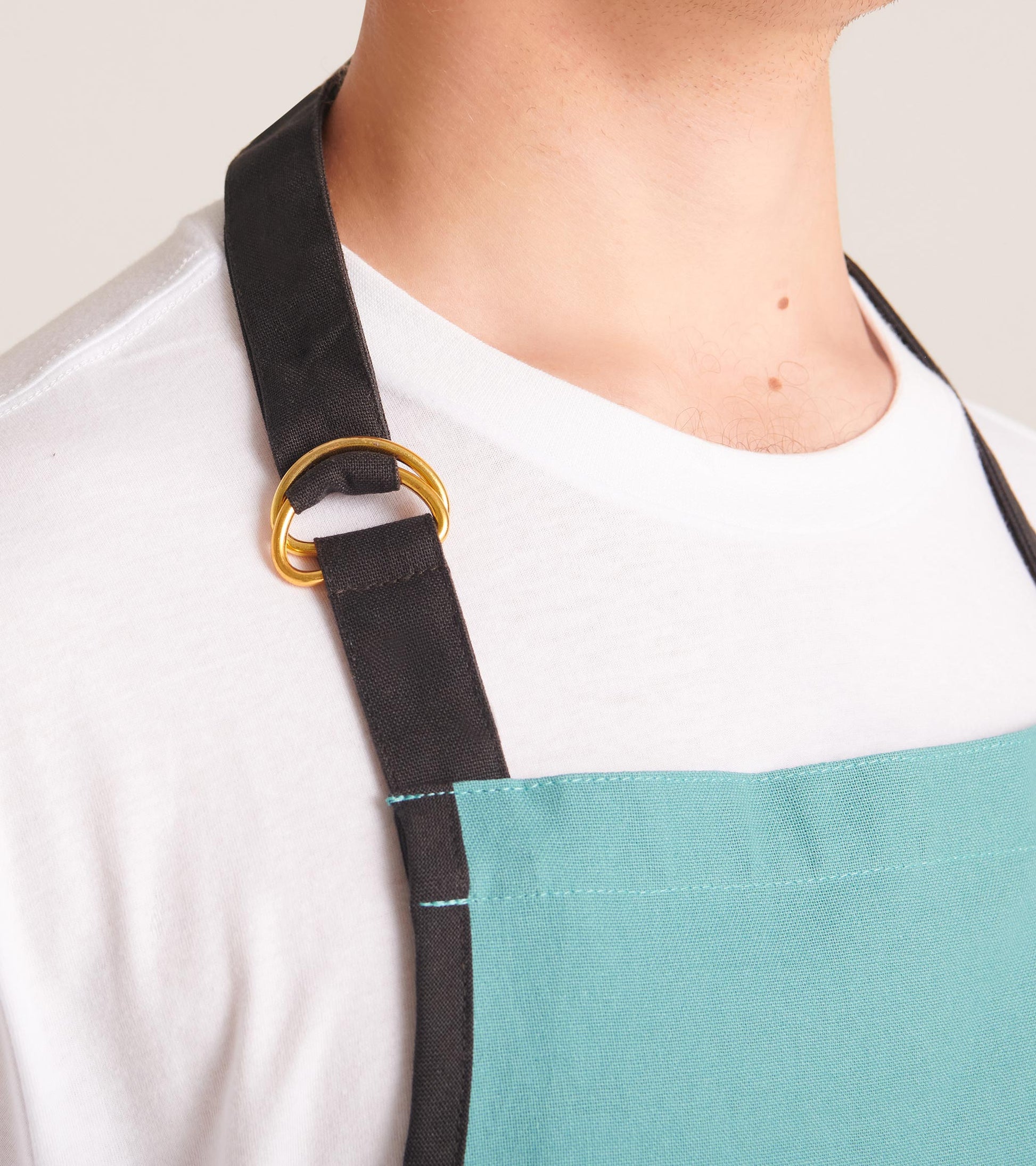 Teal apron with black straps and gold ring detail, designed for kitchen use.