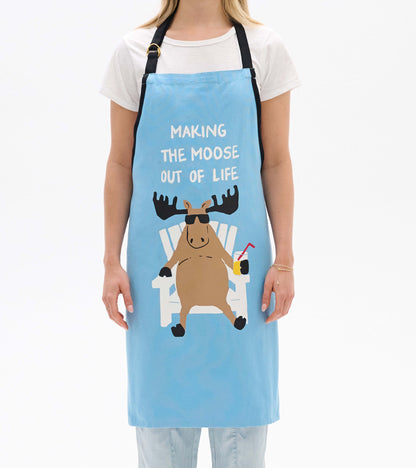 Light blue apron featuring a cartoon moose in sunglasses, sitting in a chair with a drink, ideal for cooking or crafting.