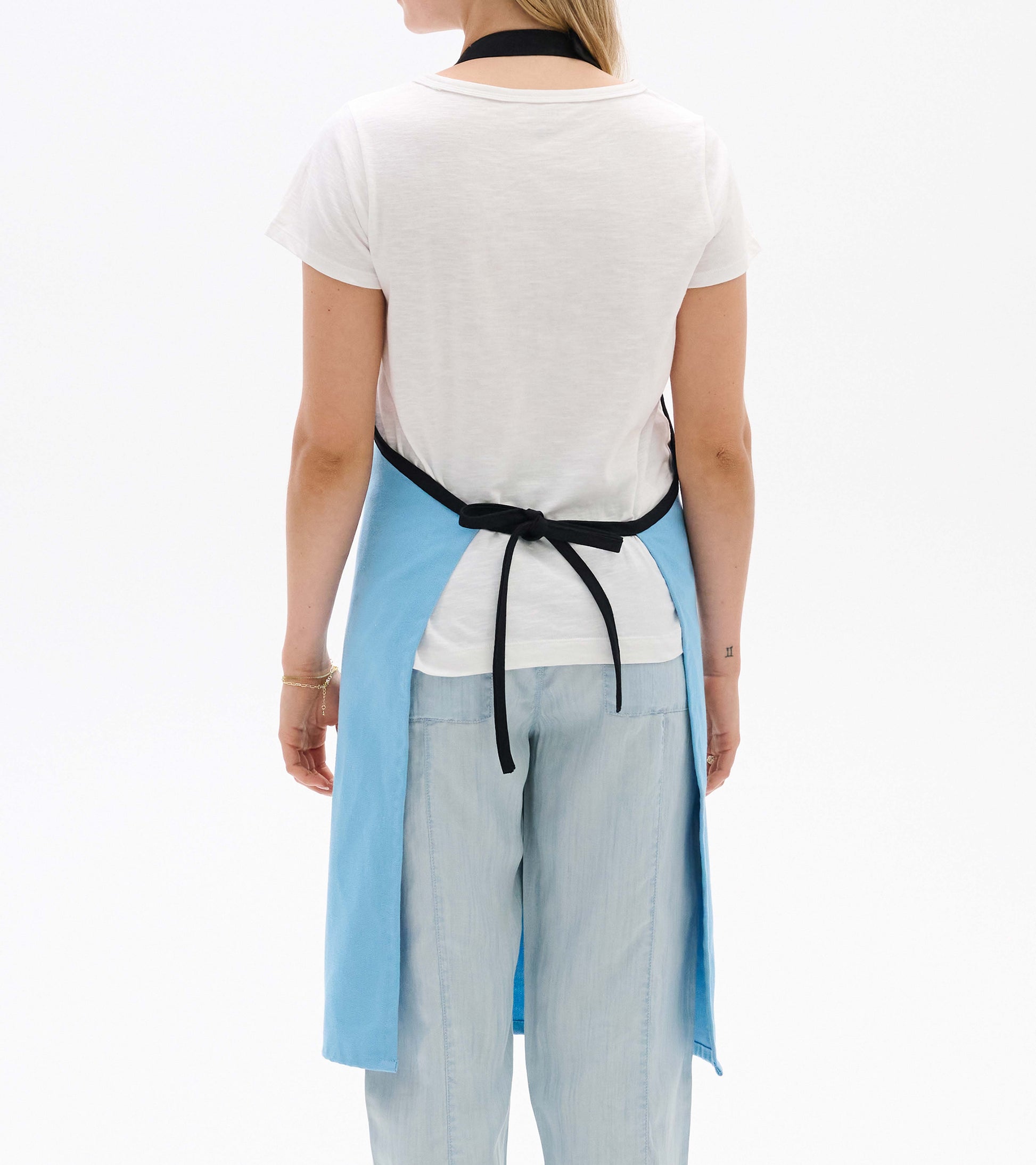 Light blue apron with a black neck strap, tied at the back, worn over a white shirt and light blue pants.