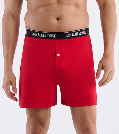 Red boxer shorts with black logo waistband and button fly, front view on a male model.