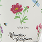 View Wildflowers Ceramic Mug - Hand-drawn pink flower with green leaves, small butterfly doodles, and the words “wild blooms” above “Mother’s Day Colle