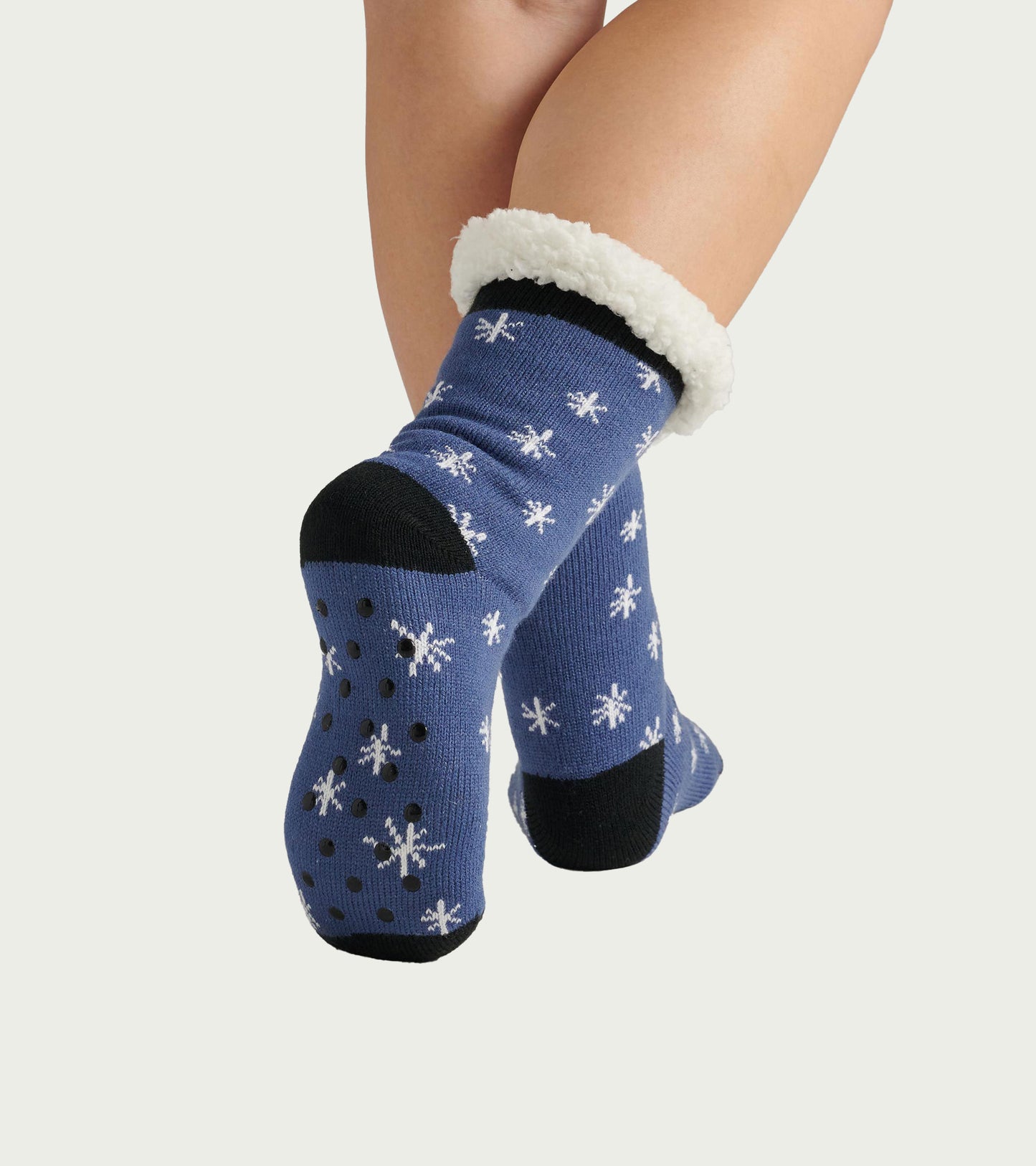 Blue sherpa-lined cabin socks with white snowflake pattern and black accents, featuring non-slip dots on the soles.