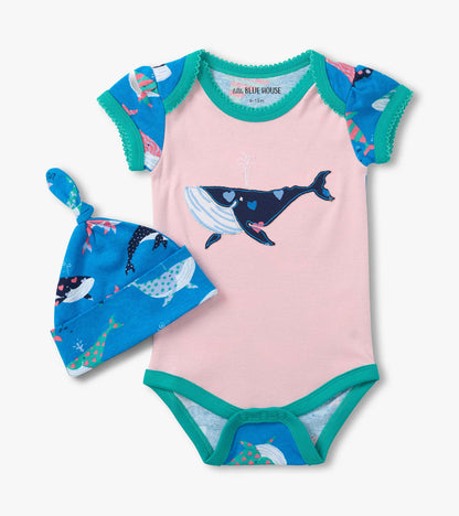 Pink baby bodysuit with teal trim, whale graphic, and matching blue whale-print hat, front view