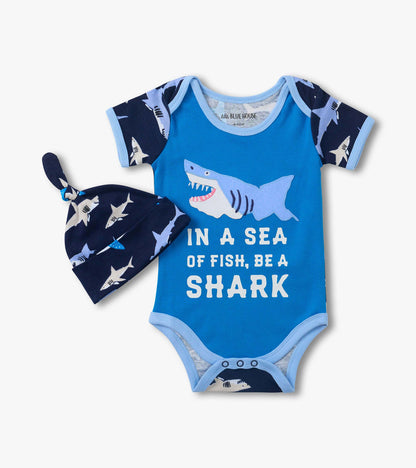 Blue baby bodysuit with shark graphic and matching navy shark-print hat, front view