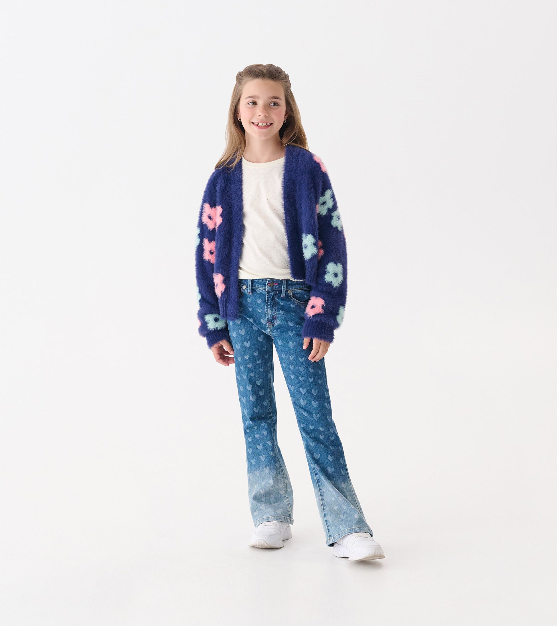 Flared leg denim for girls featuring a heart pattern in blue, paired with a cozy cardigan and white sneakers.