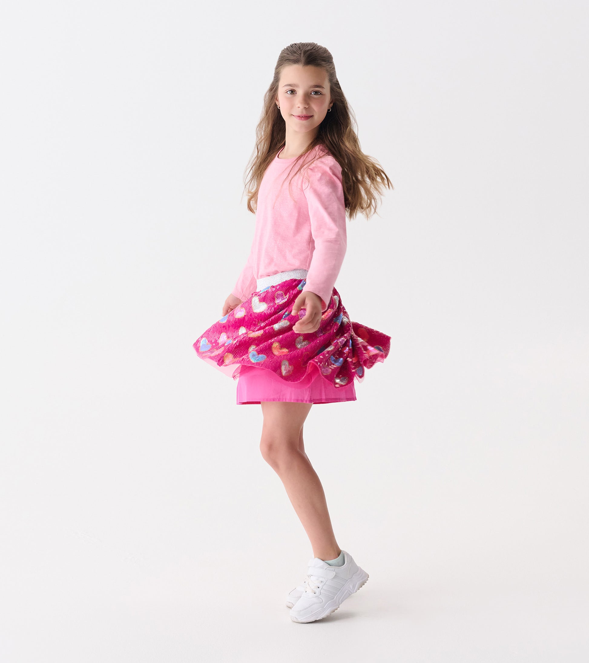 Light pink puff sleeve graphic tee worn by a girl, paired with a vibrant pink skirt featuring heart patterns.