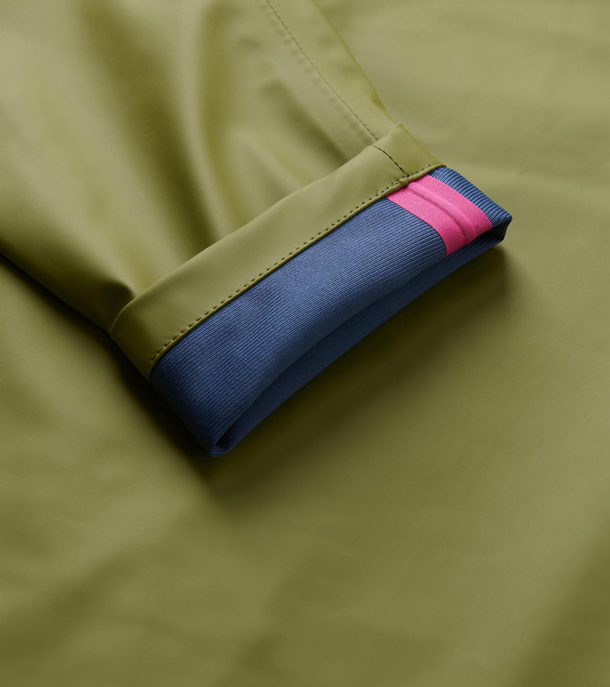 Close-up of loden green rain jacket sleeve with blue ribbed inner cuff and pink stripe
